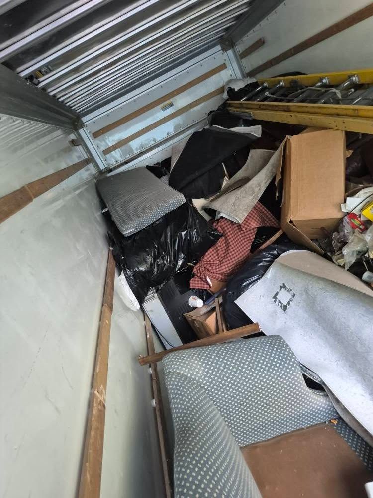 A cluttered storage unit with furniture, trash bags, and cardboard boxes.