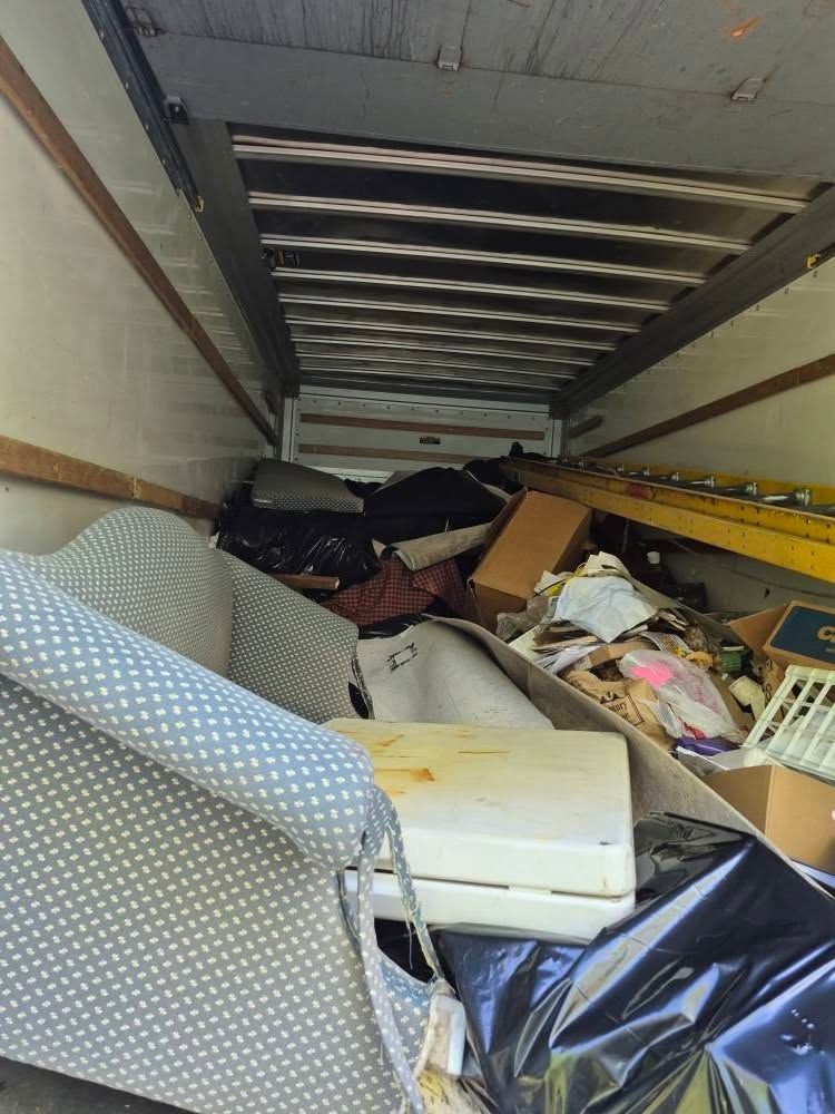Interior of a cluttered moving truck filled with furniture, boxes, and trash.