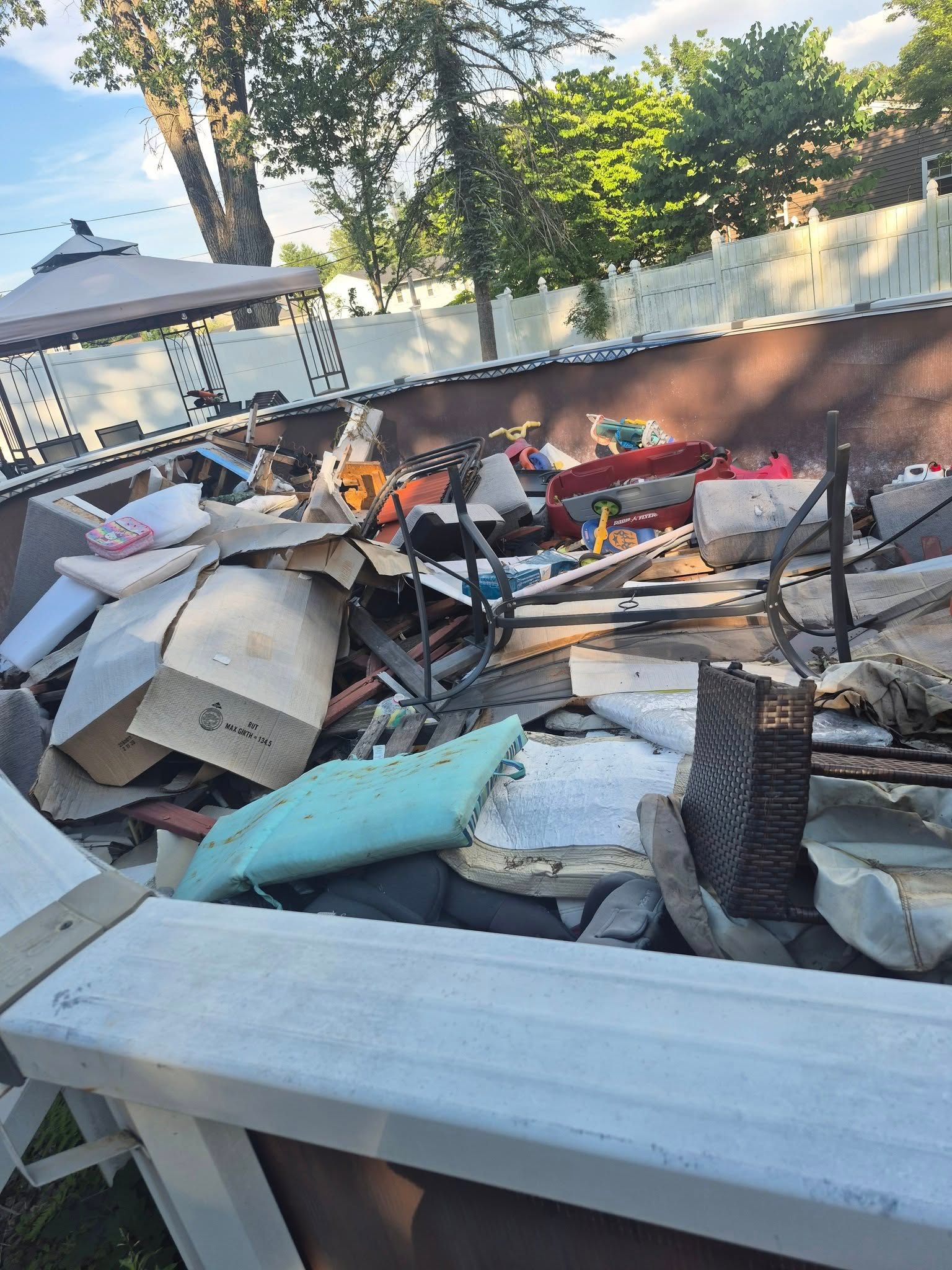 Debris pile in a backyard, including cardboard boxes, furniture, and construction materials.