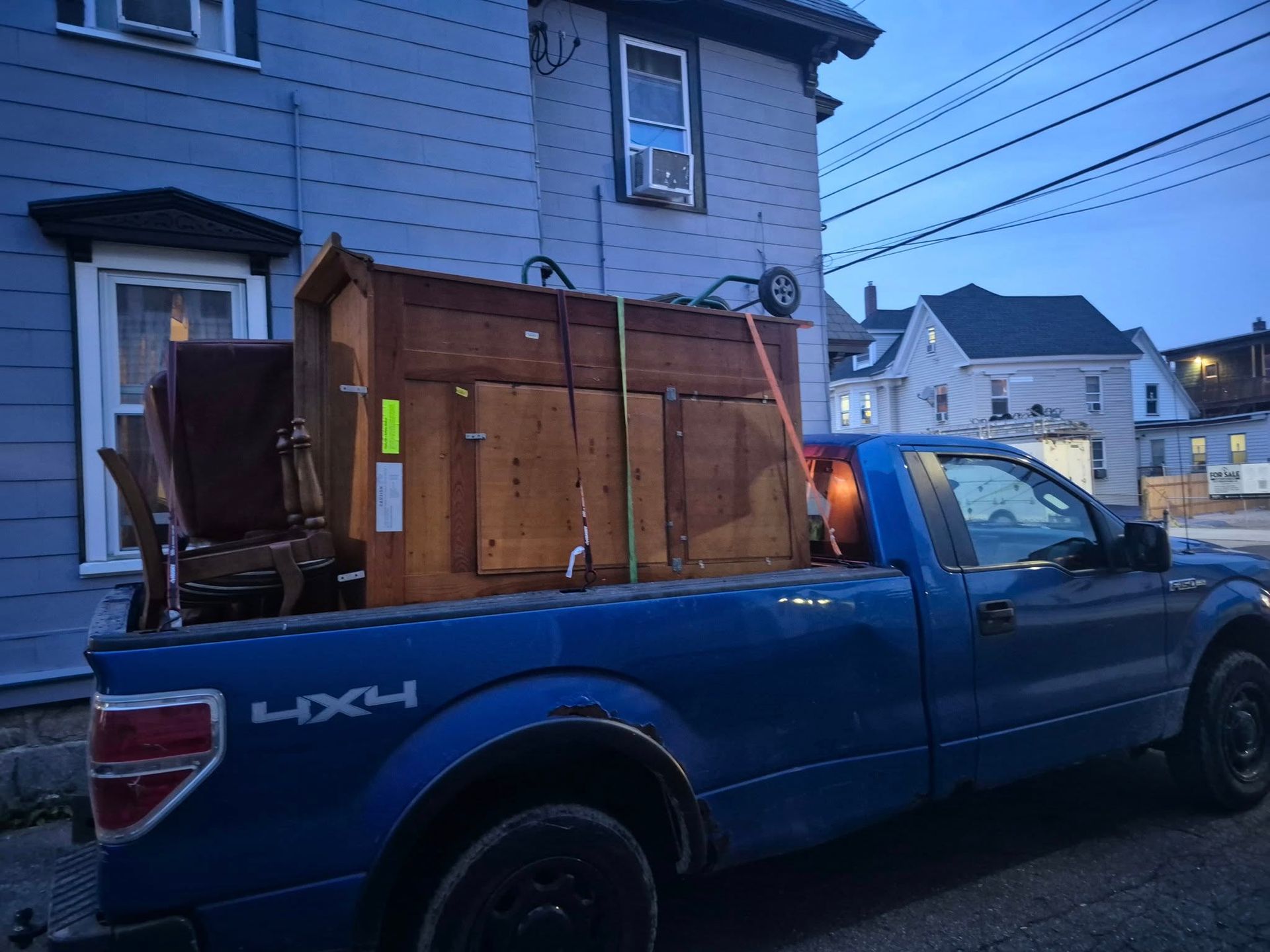 Blue pickup truck with furniture loaded in the back on a residential street.
