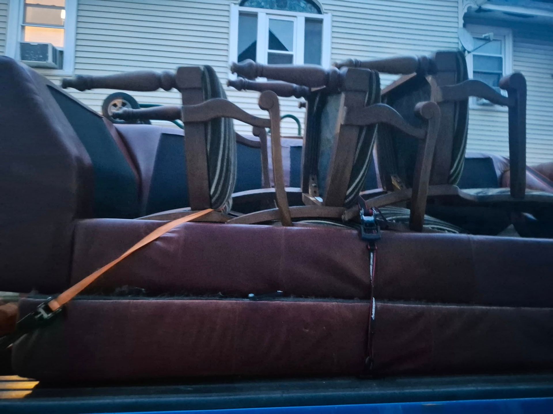 Chairs and a table strapped to a red couch in a pickup truck bed; house background.