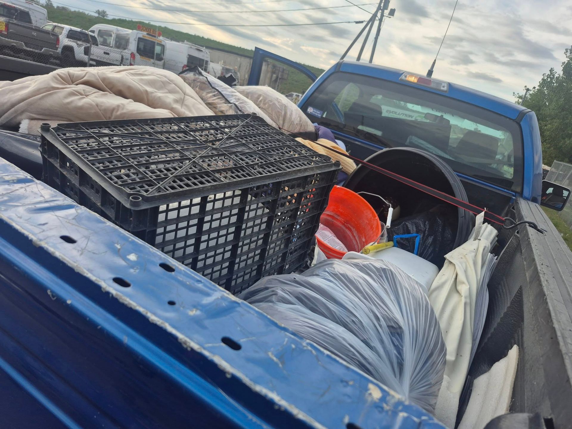 Blue truck bed loaded with various items, including a crate, bucket, and bags.