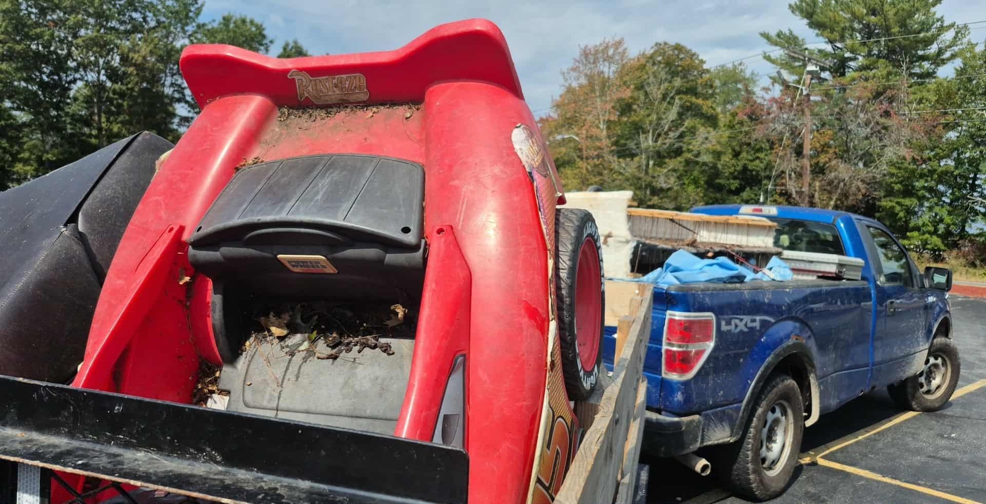 Red machine and debris in a truck bed, blue pickup truck in a parking lot.