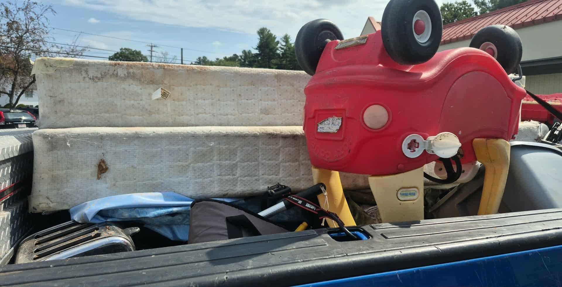 Truck bed filled with junk, including a red toy car and dirty mattress.