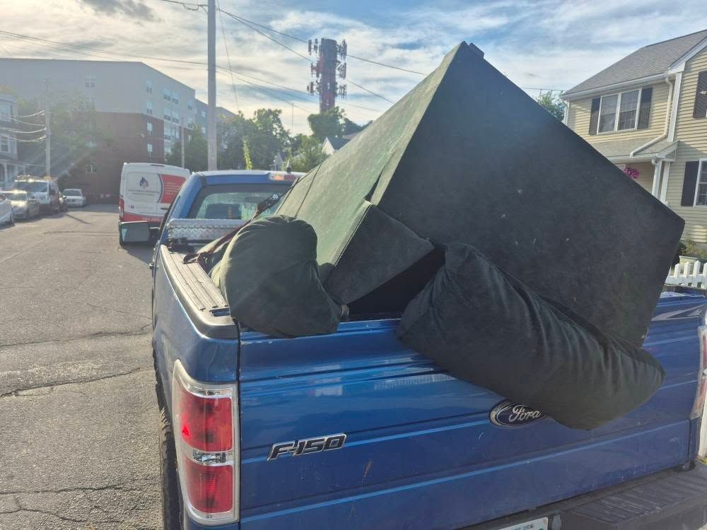 Blue pickup truck transporting a large, black sofa down a residential street.