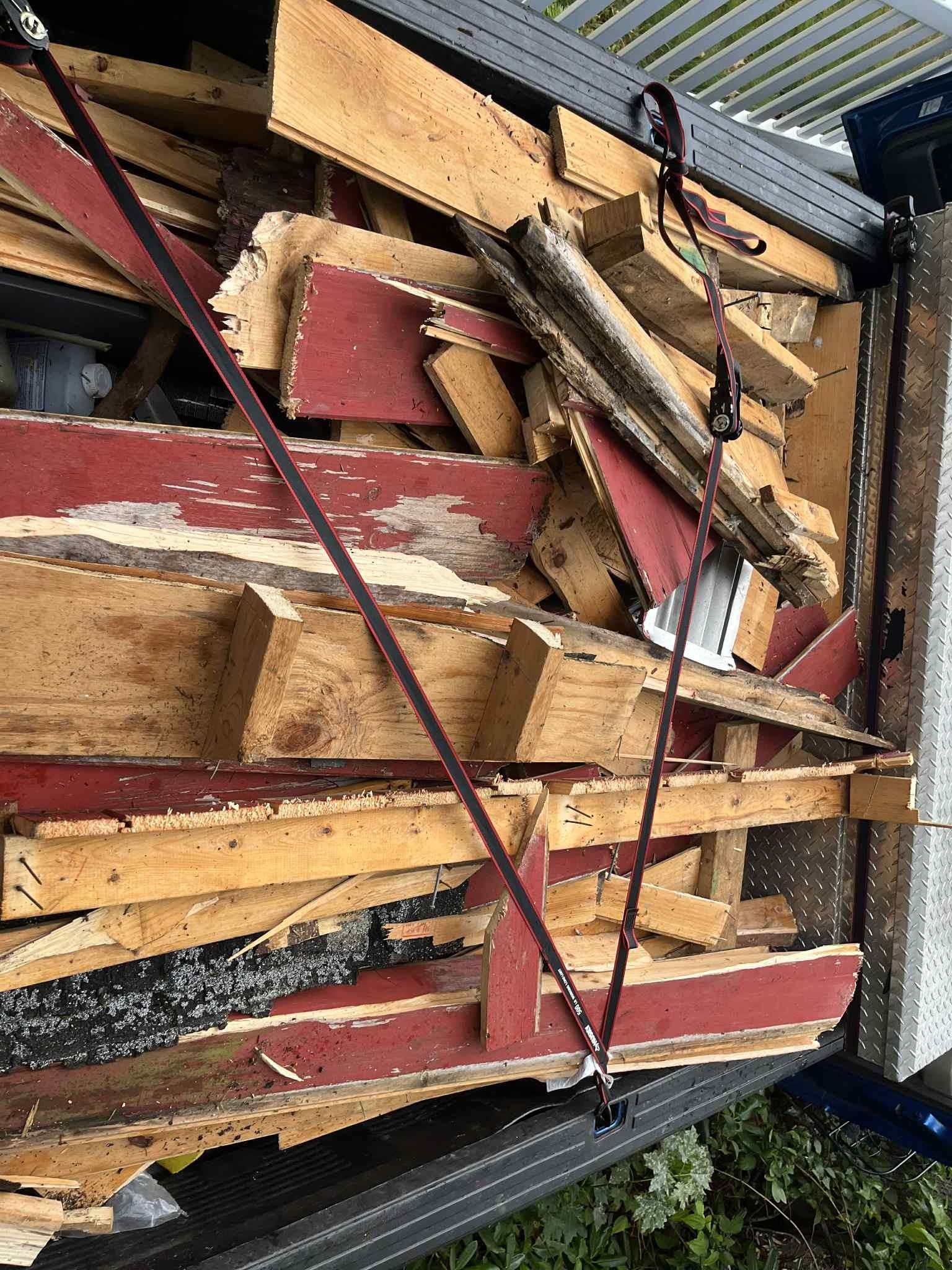 Pile of red and yellow wood scraps secured with straps in a truck bed.