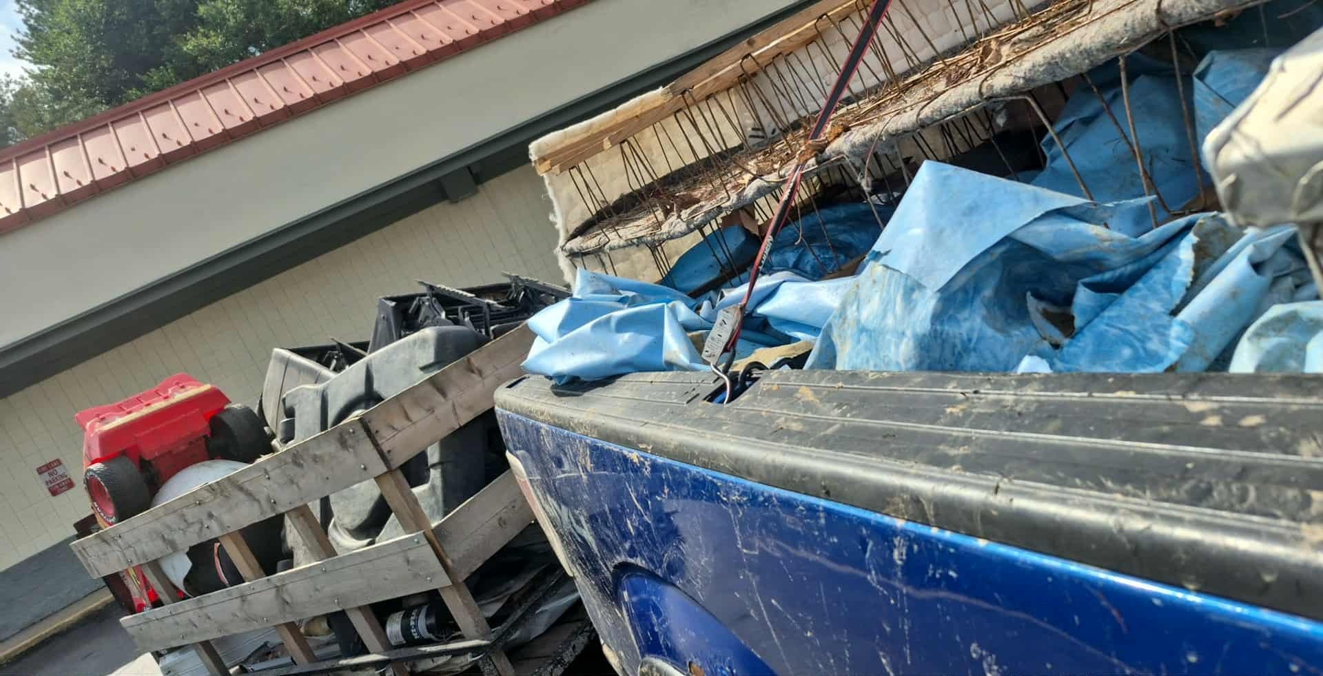 Blue truck bed overflowing with trash bags, near a building with red trim.