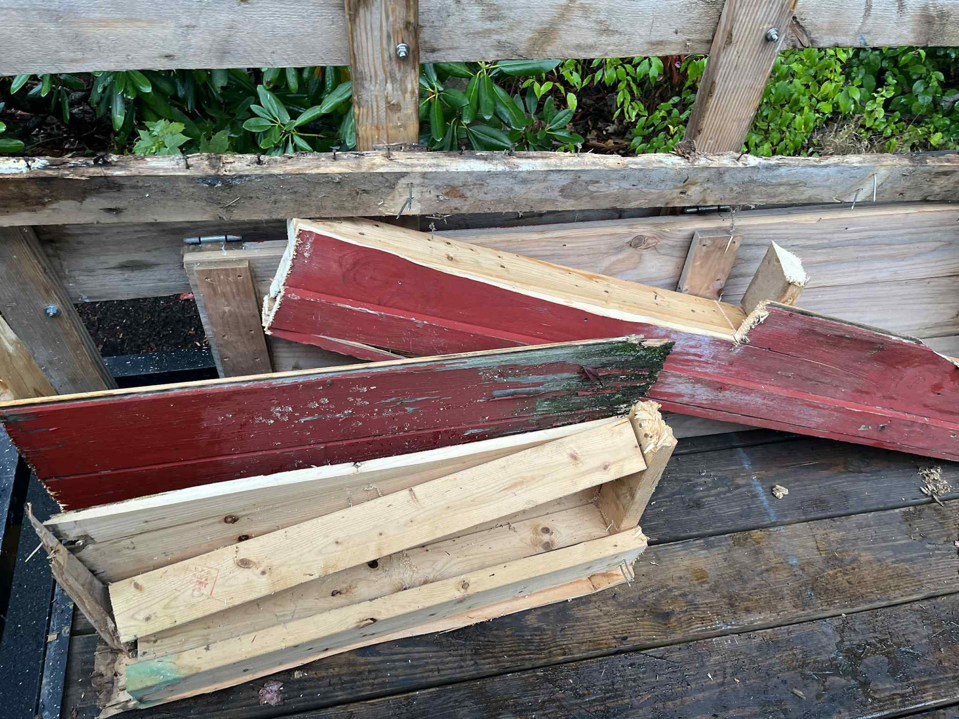 Deconstructed wooden planters on a wooden surface, some painted red, others unpainted with some green.