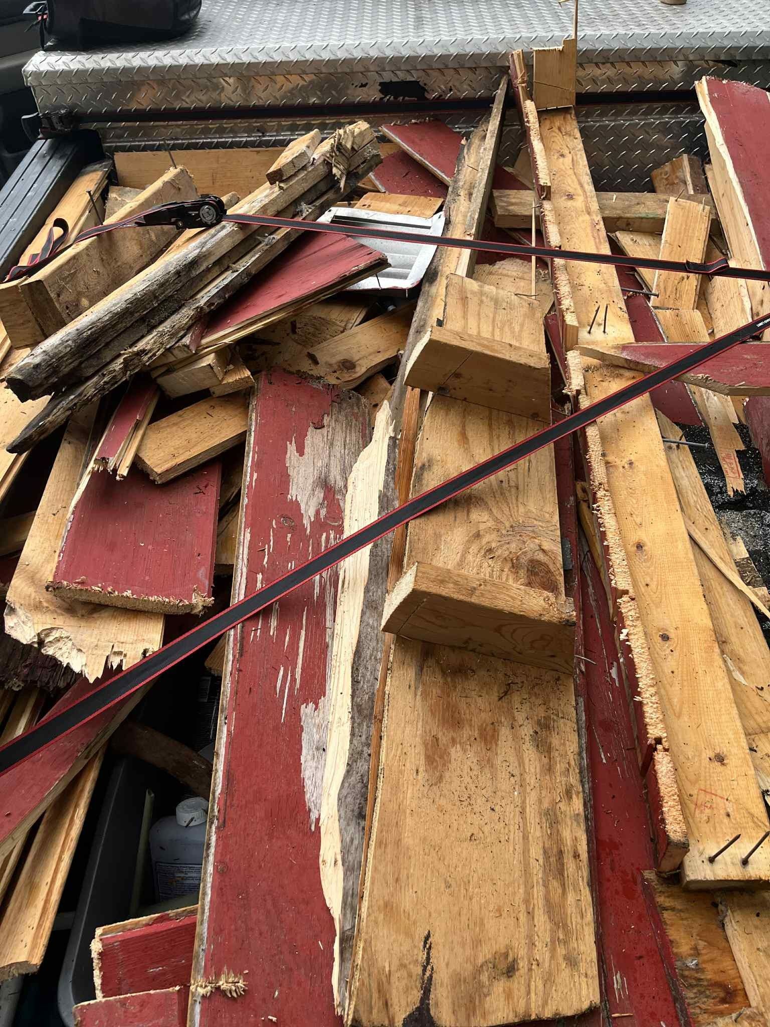 Pile of discarded wood and red-painted planks inside a vehicle, secured with straps.