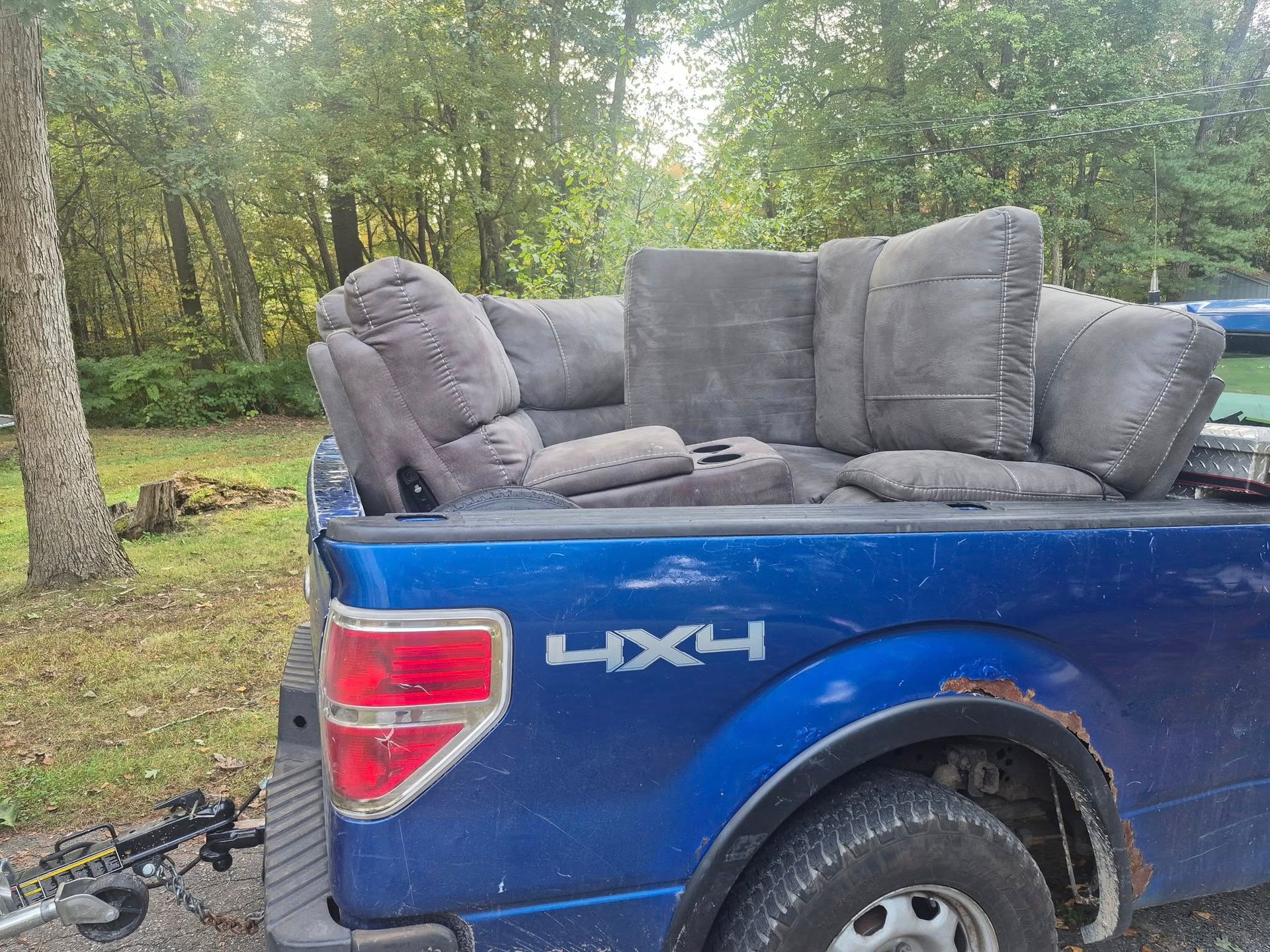 Blue pickup truck bed filled with gray cushions and pillows. Rust visible on the fender. Outdoors.