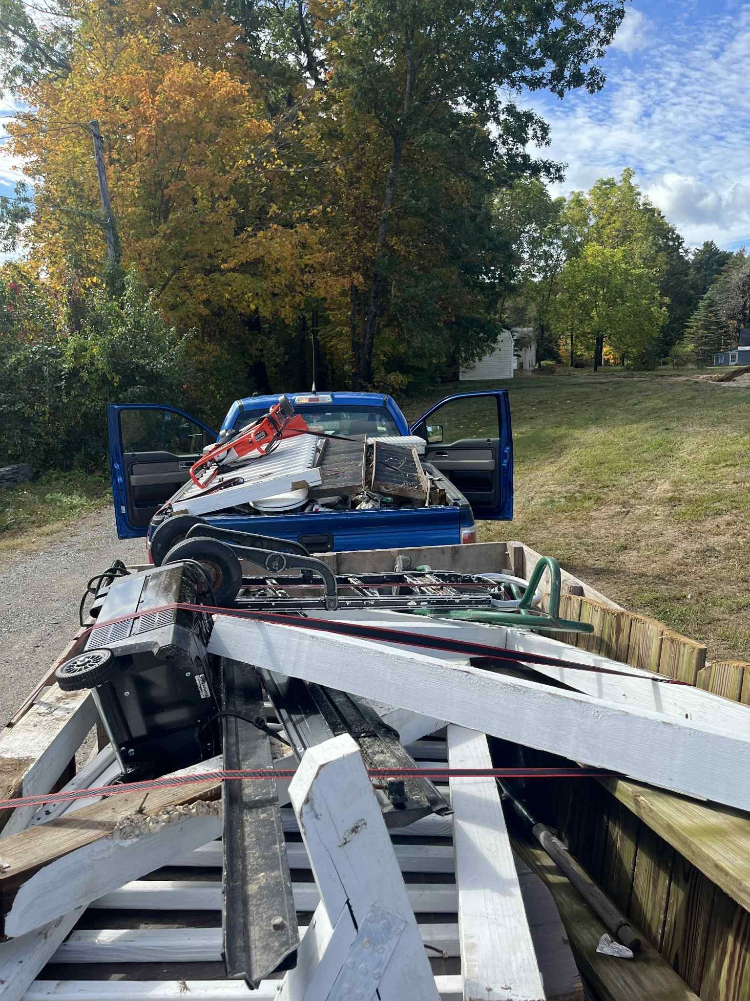 Blue pickup truck loaded with white fencing and equipment in a yard on a sunny day.