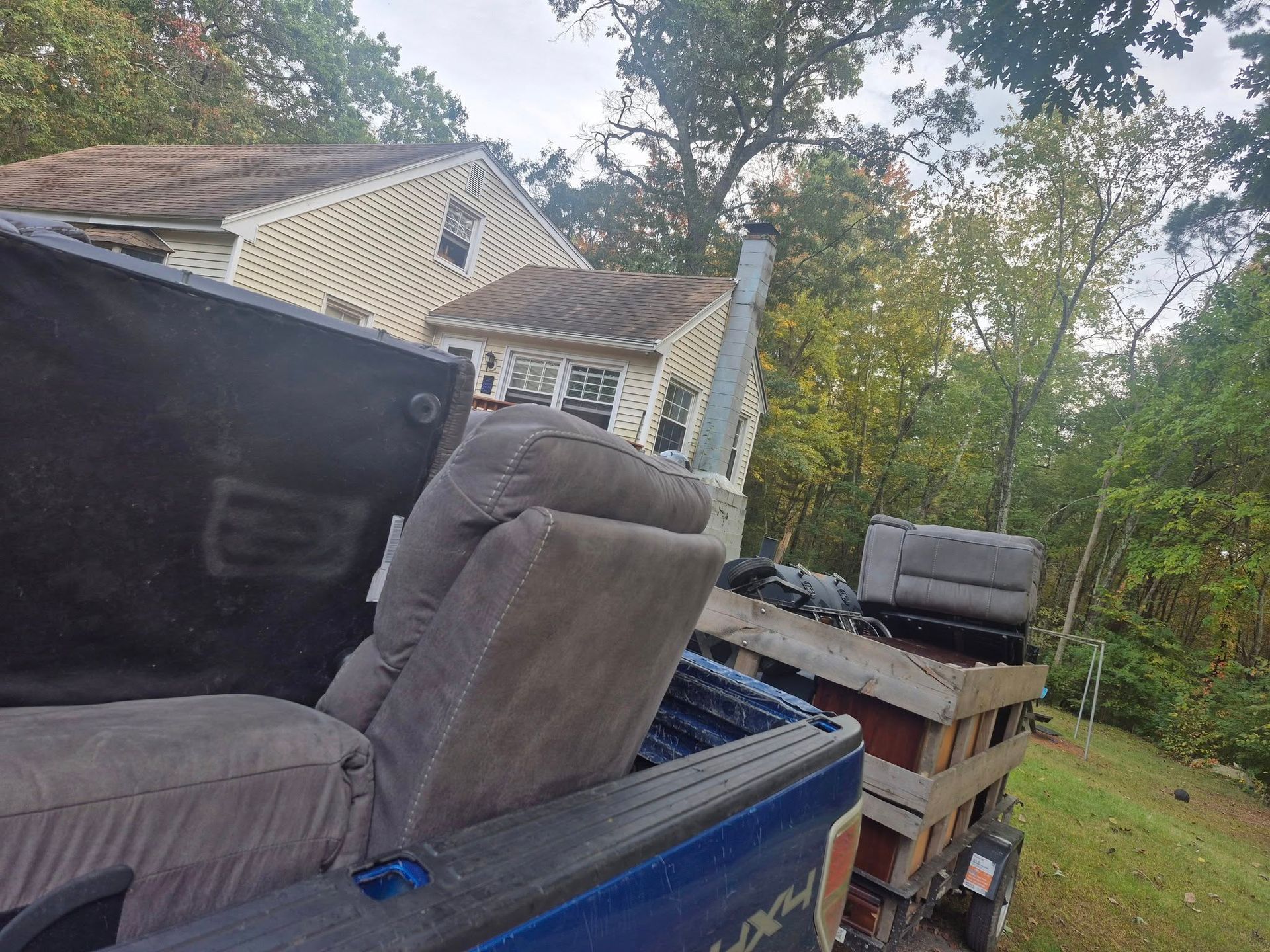 Truck bed loaded with furniture in front of a house surrounded by trees.