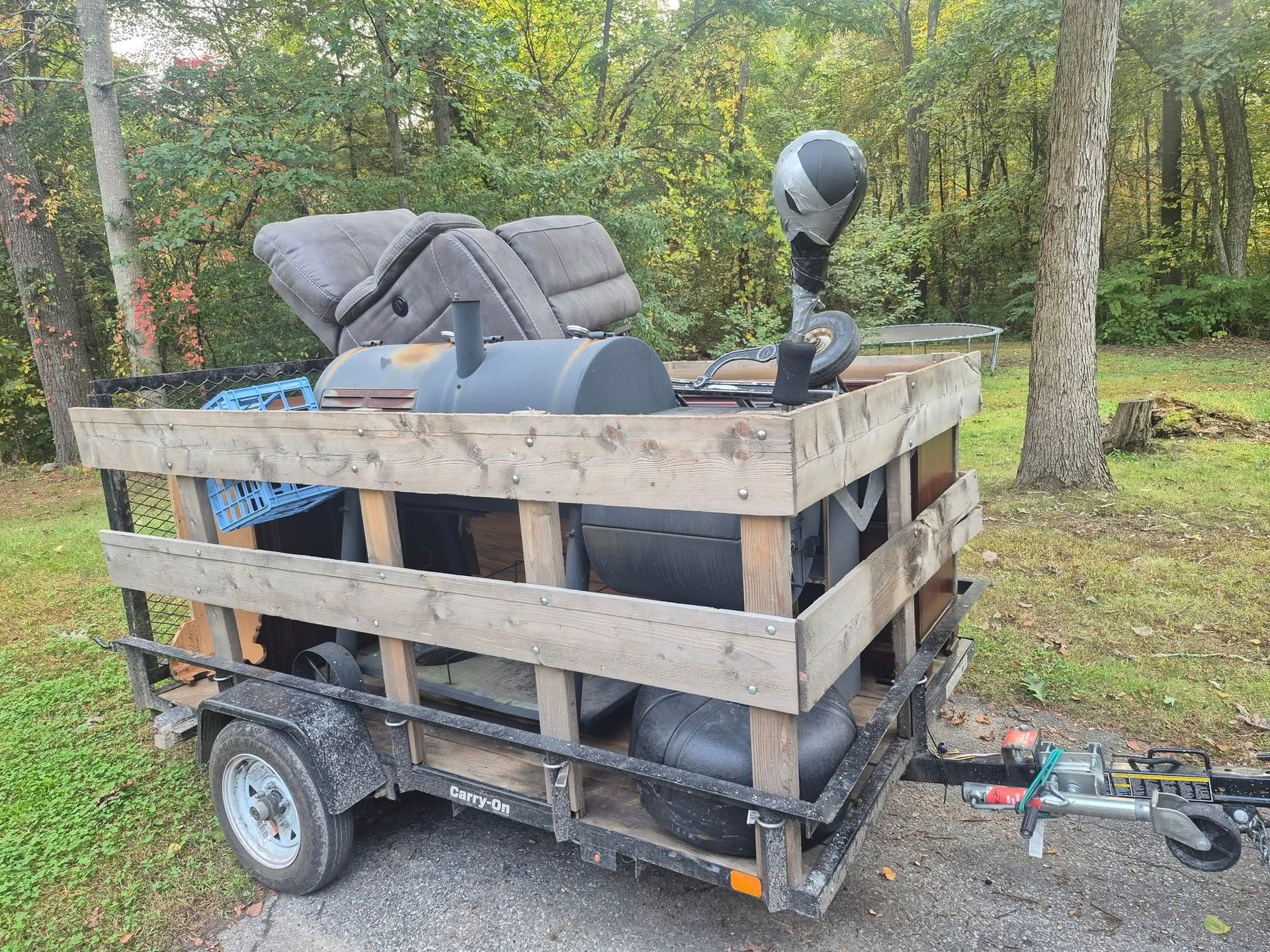 Trailer loaded with furniture and yard equipment parked outdoors near trees.