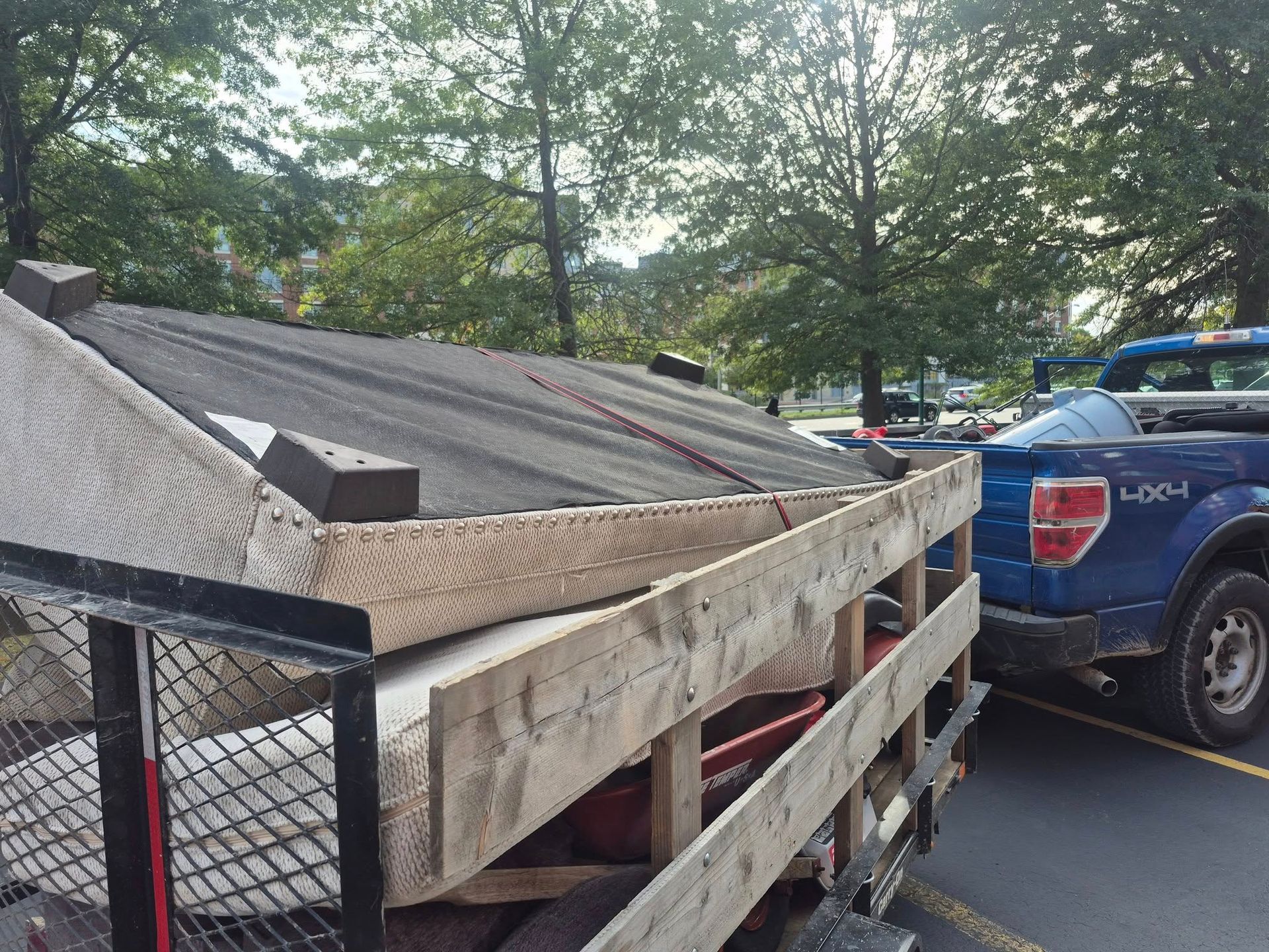 A trailer loaded with construction materials next to a blue pickup truck in a parking lot.