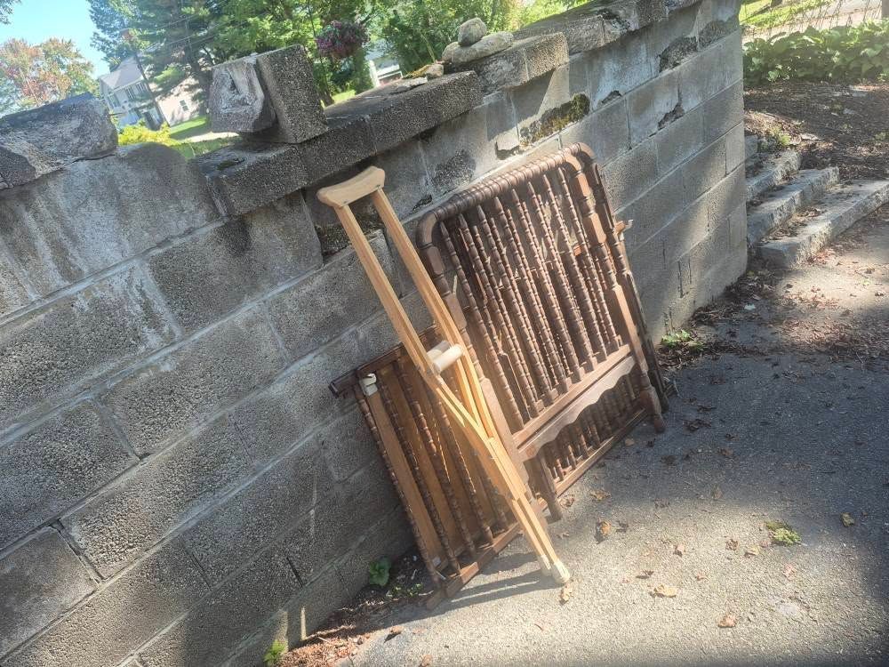 Crutches and a metal crib frame leaning against a weathered concrete wall on a sunny day.