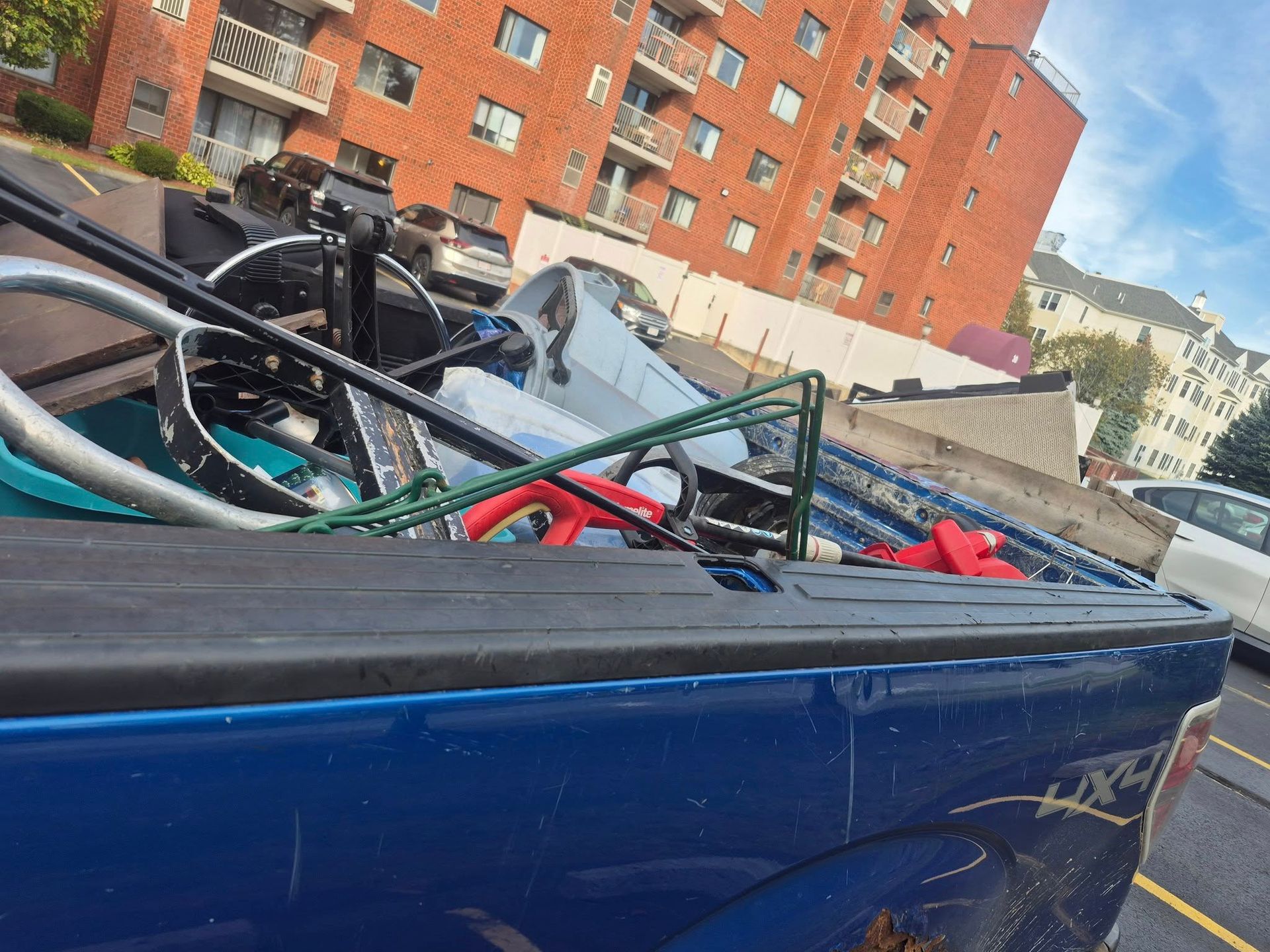 Blue pickup truck bed filled with scrap metal, parked in front of a brick building.