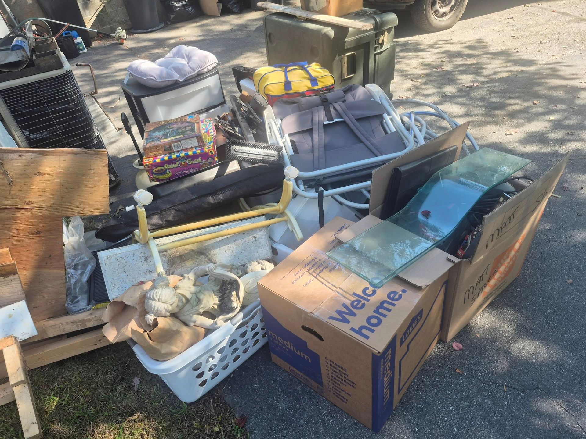Pile of discarded household items, including boxes, chair, and glass, on a driveway.