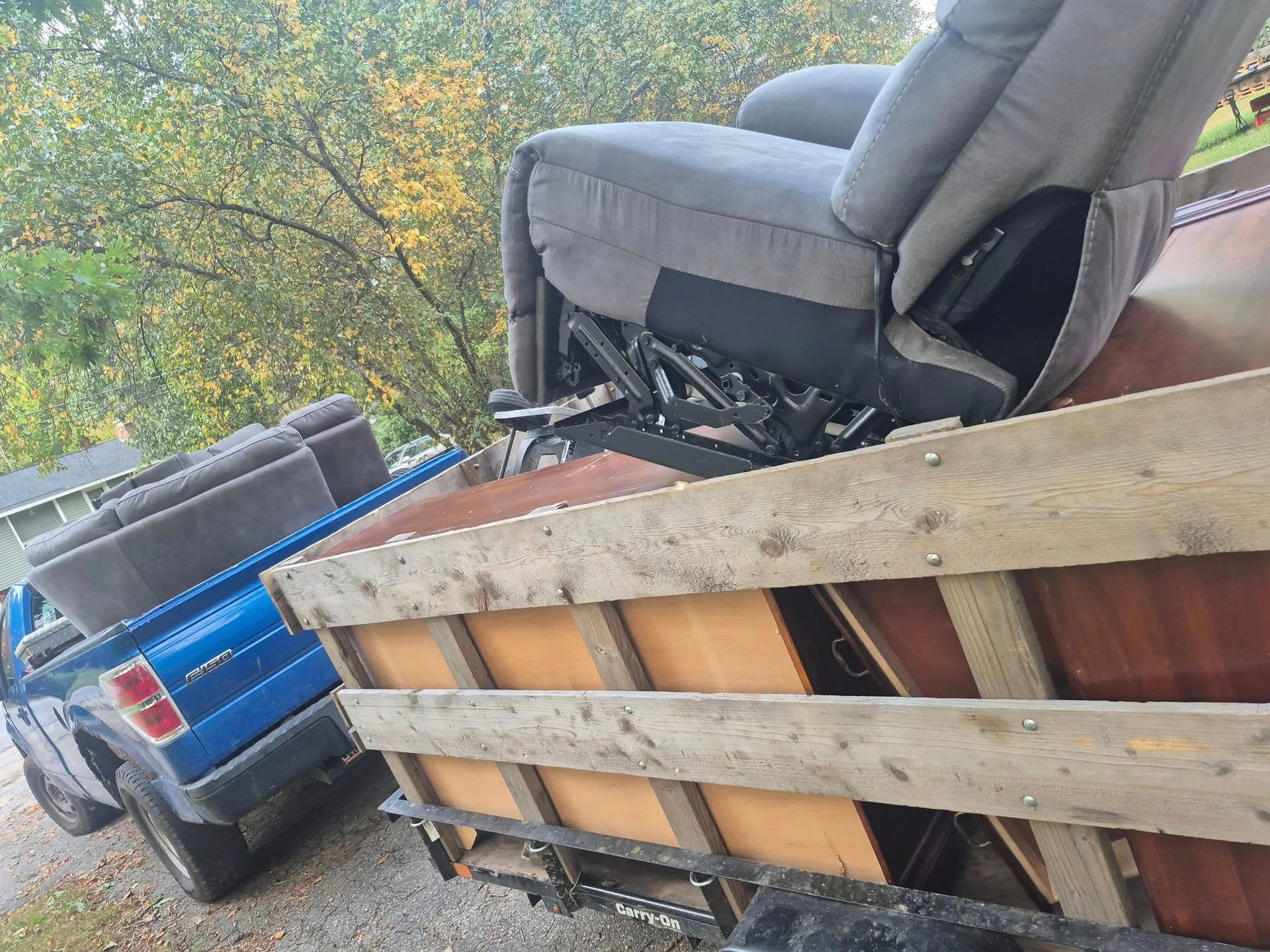 Blue truck towing a trailer loaded with gray recliner and couch, in a residential setting.