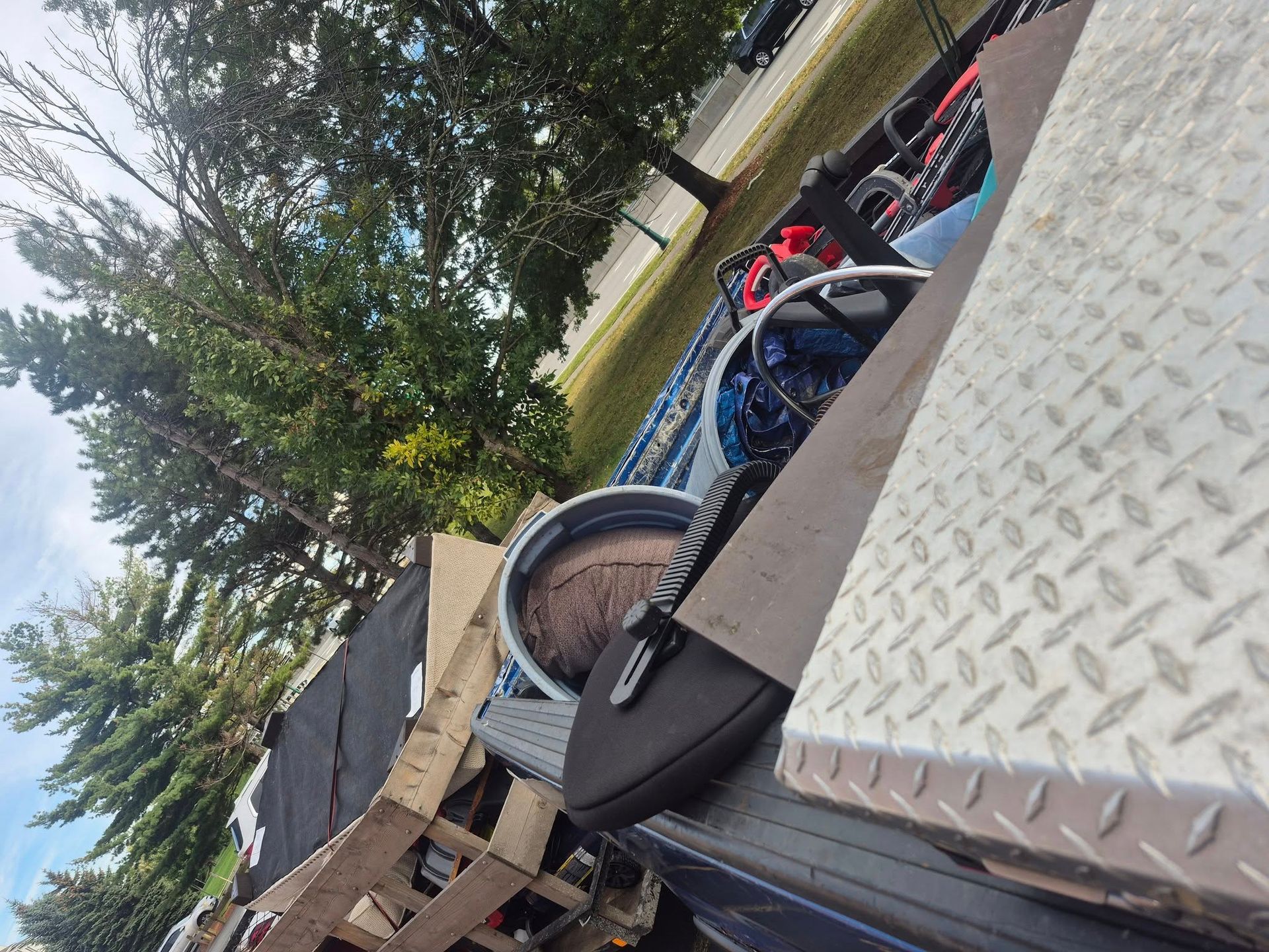 Truck bed with metal surfaces, containing equipment and a tree visible in the background.