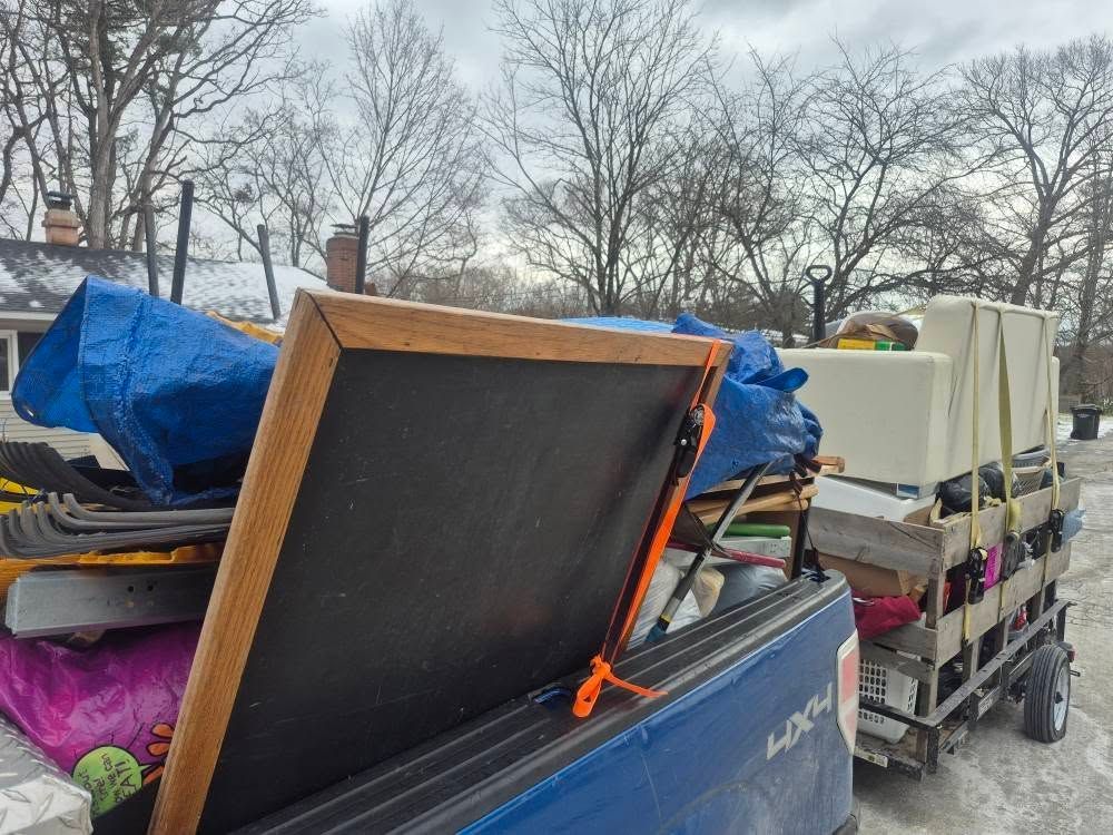 Fallen shed on dark asphalt next to a wooden fence and a yellow house. Debris scattered around.