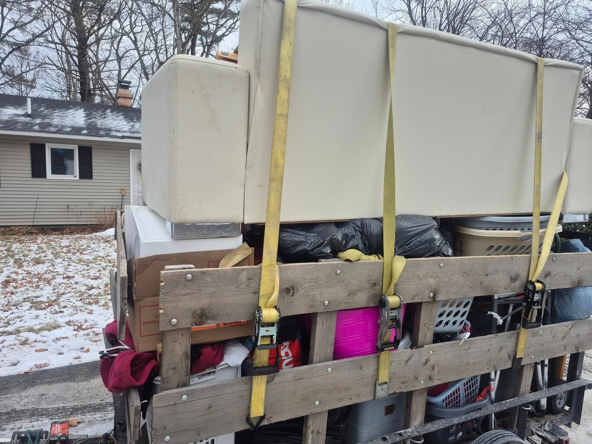 Fallen shed on dark asphalt next to a wooden fence and a yellow house. Debris scattered around.