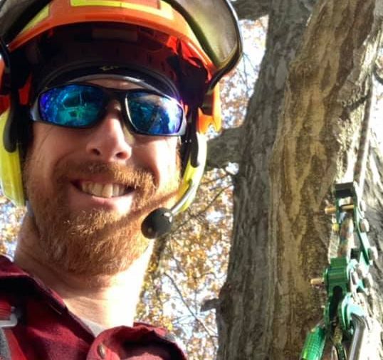 A white utility truck with a boom lift is parked on a residential driveway, with its front wheels lifted off the ground.