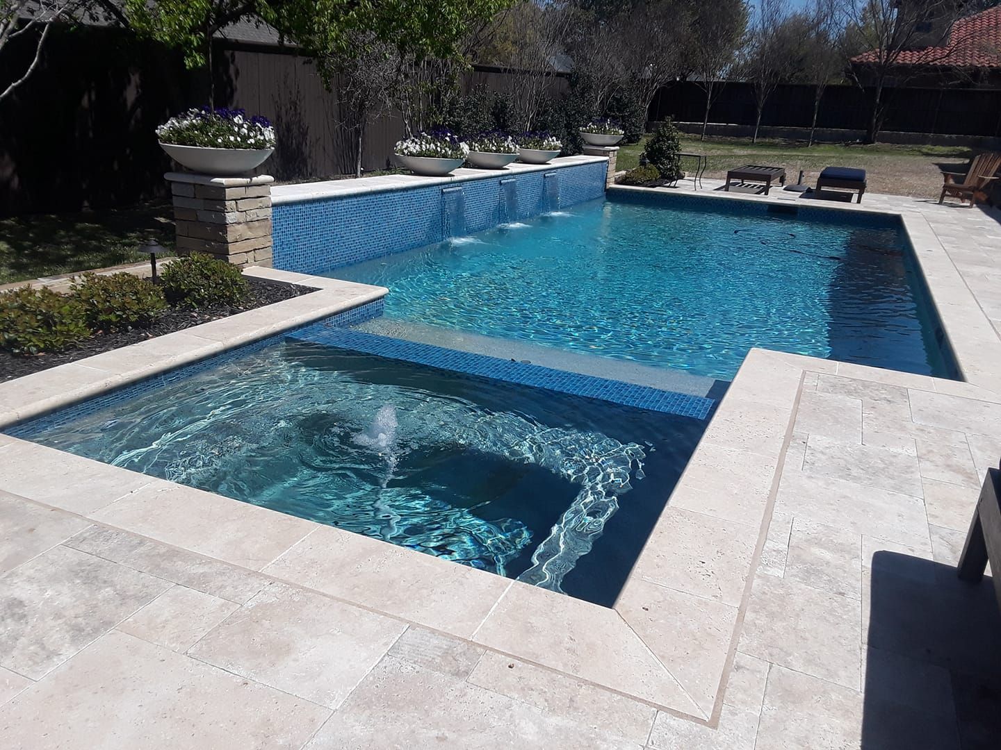 Swimming pool with raised spa, stone patio, blue tile, and water feature.