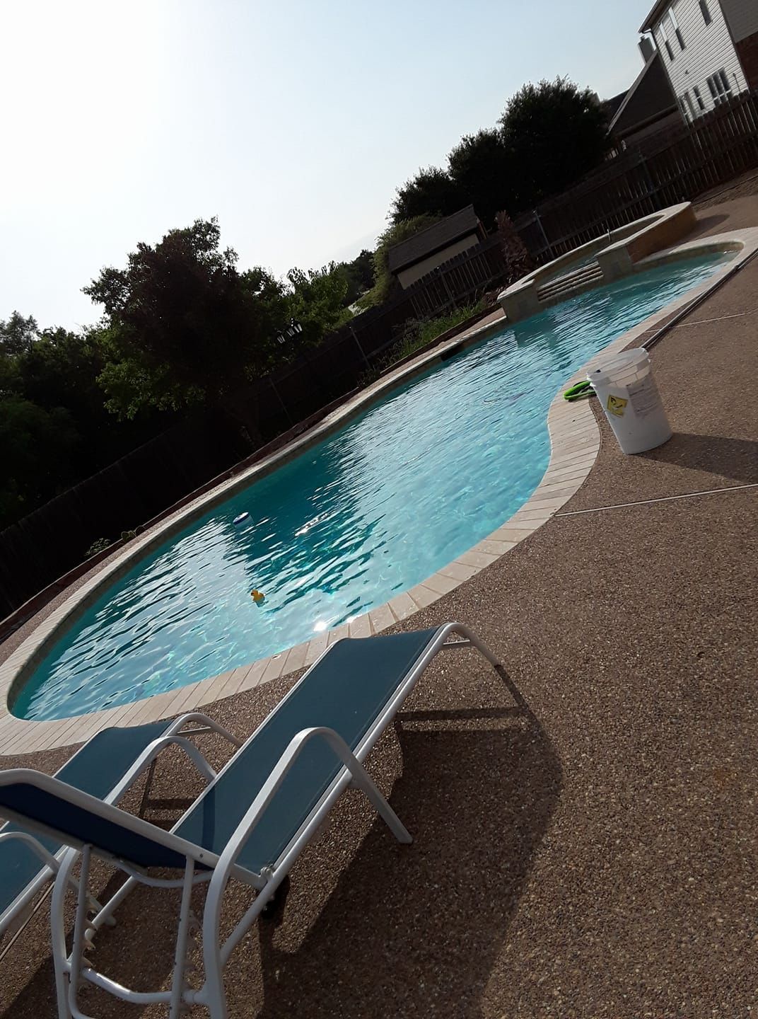 Pool with blue water and two lounge chairs on a sunny day.