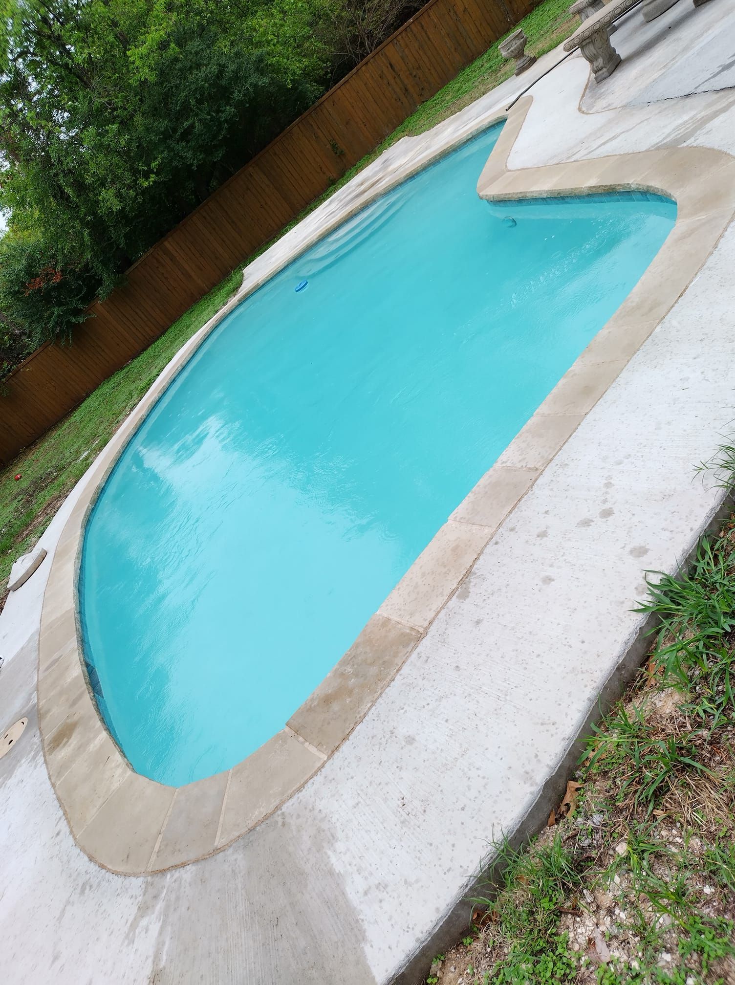 Swimming pool with turquoise water and concrete border, surrounded by grass.