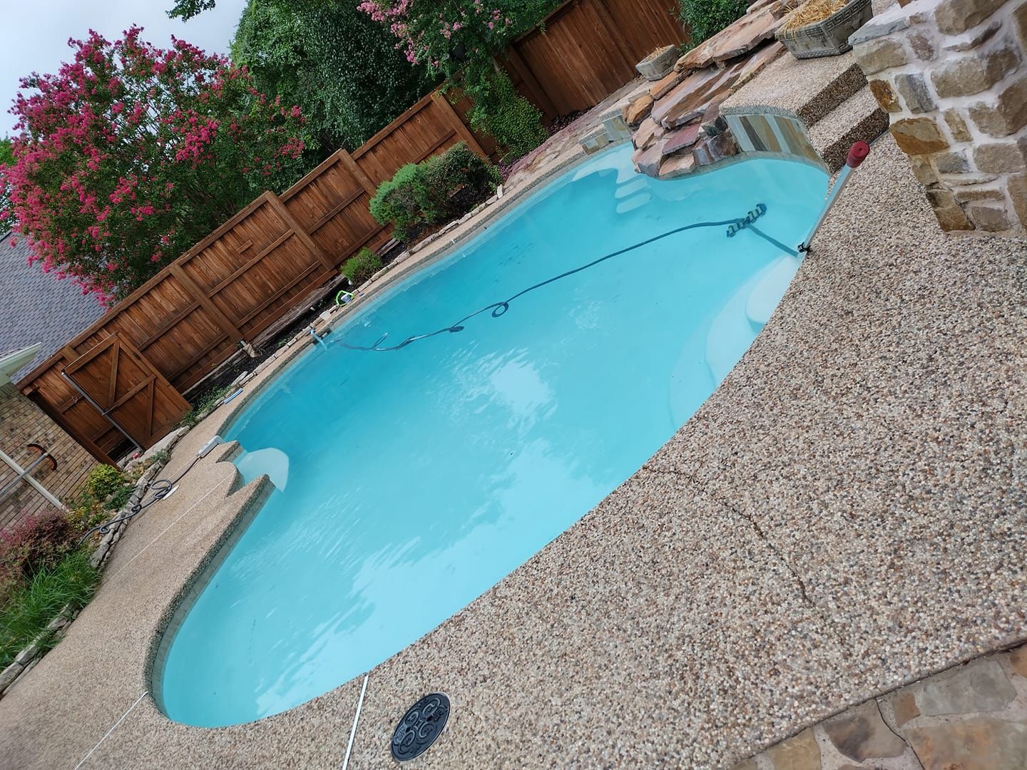 A turquoise pool surrounded by textured concrete patio with a wooden fence in the background.
