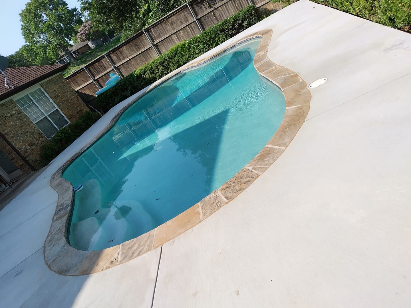 Pool with light blue water and tan stone edging, surrounded by gray concrete patio.