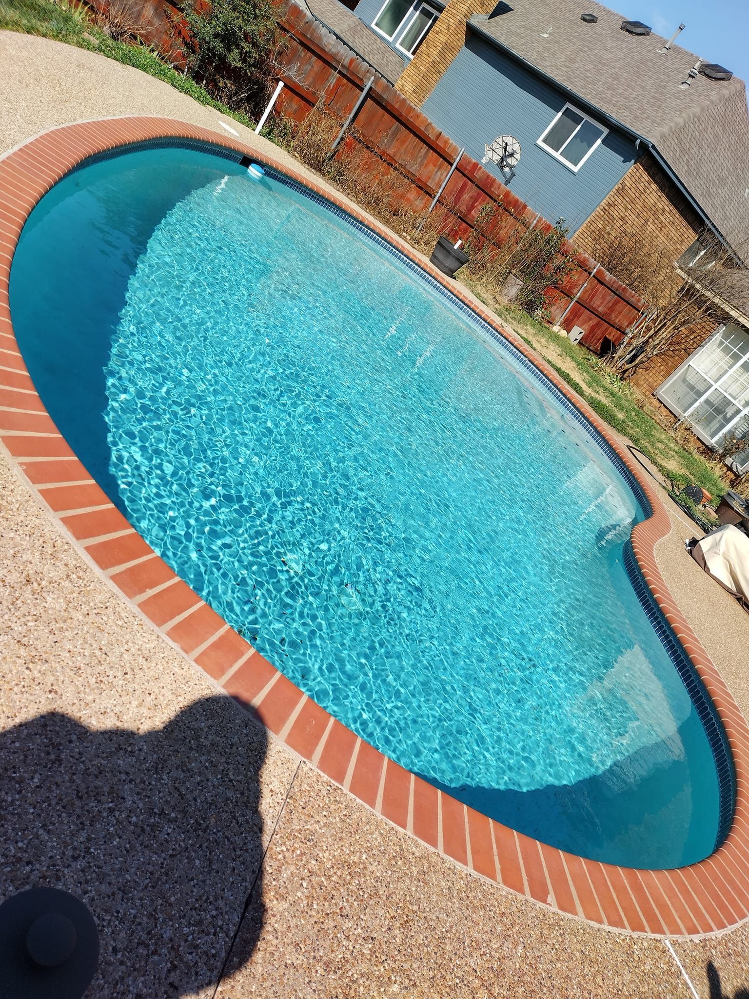 Oval-shaped swimming pool with brick edging, filled with turquoise water.