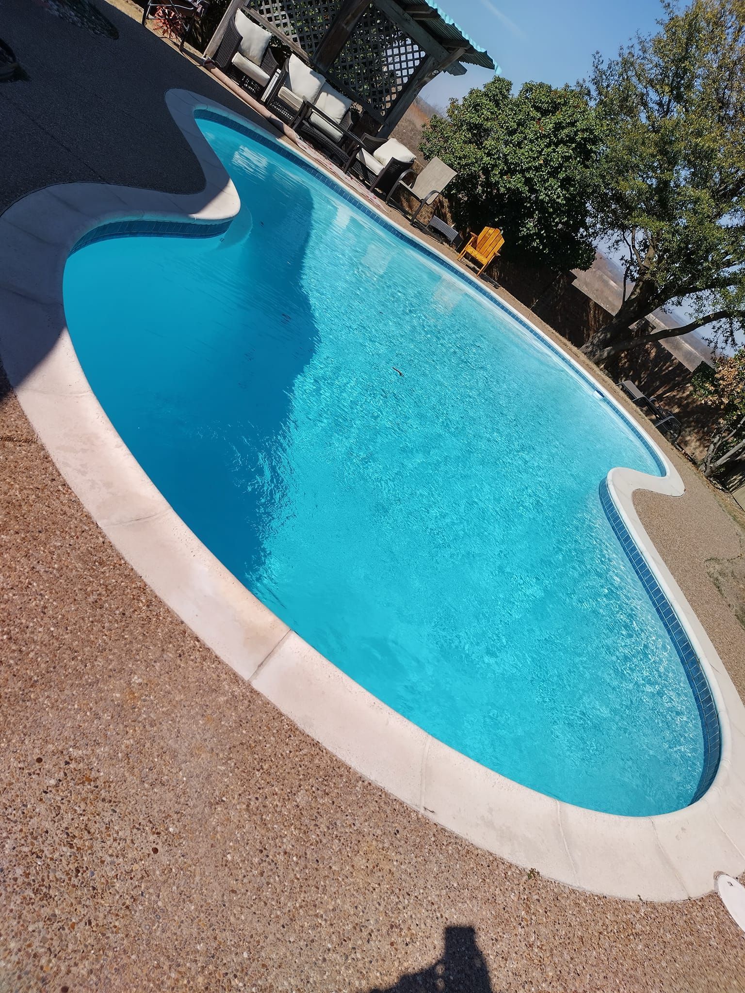 Pool filled with clear blue water, surrounded by tan concrete and outdoor seating area.