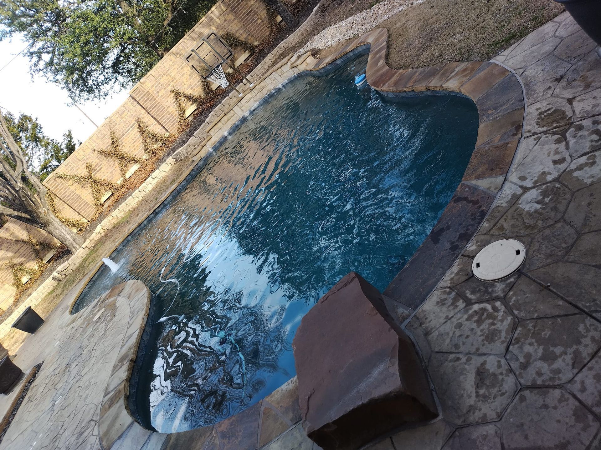 A small, kidney-shaped pool with stone coping and surrounding patio.