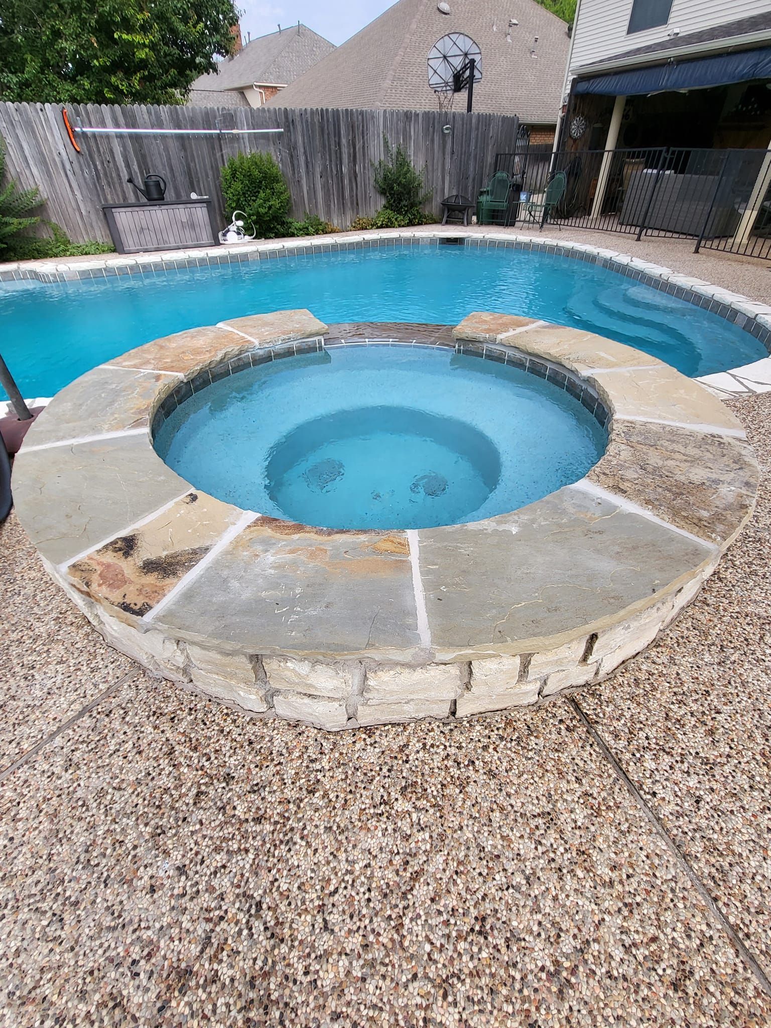 Swimming pool with connected hot tub, stone surround, and concrete decking in backyard setting.