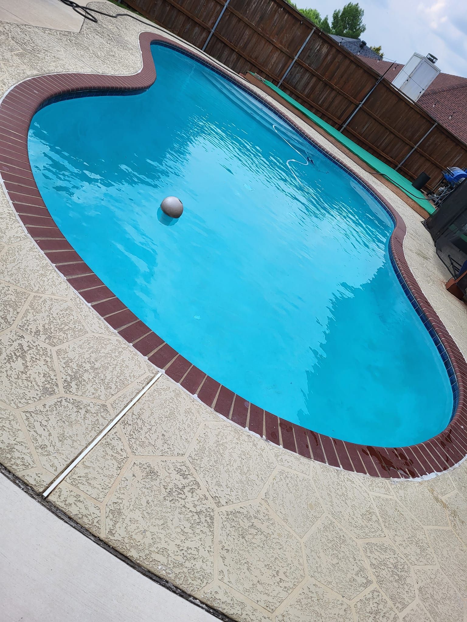 Blue swimming pool with brown border and white deck, a ball floats on the water.
