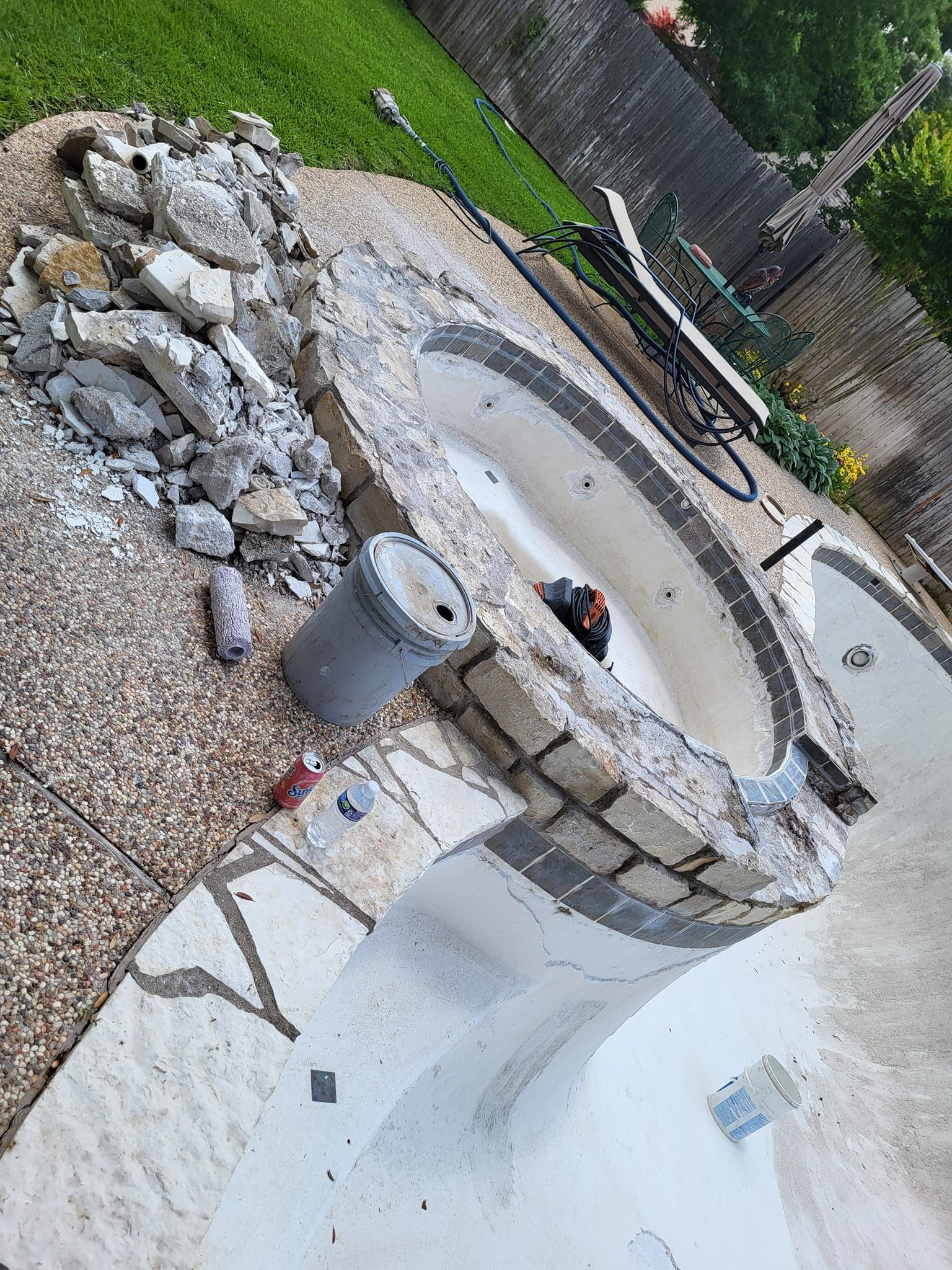 Pool undergoing renovation; broken stone border, debris pile, tools visible, empty pool basin.