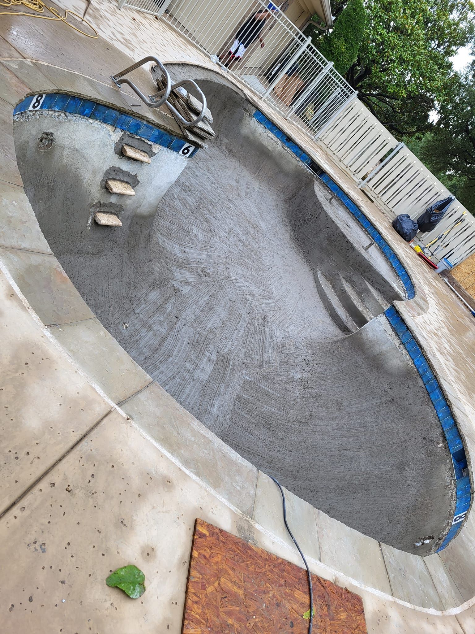 Empty concrete swimming pool under construction, blue tile border, outdoor setting.