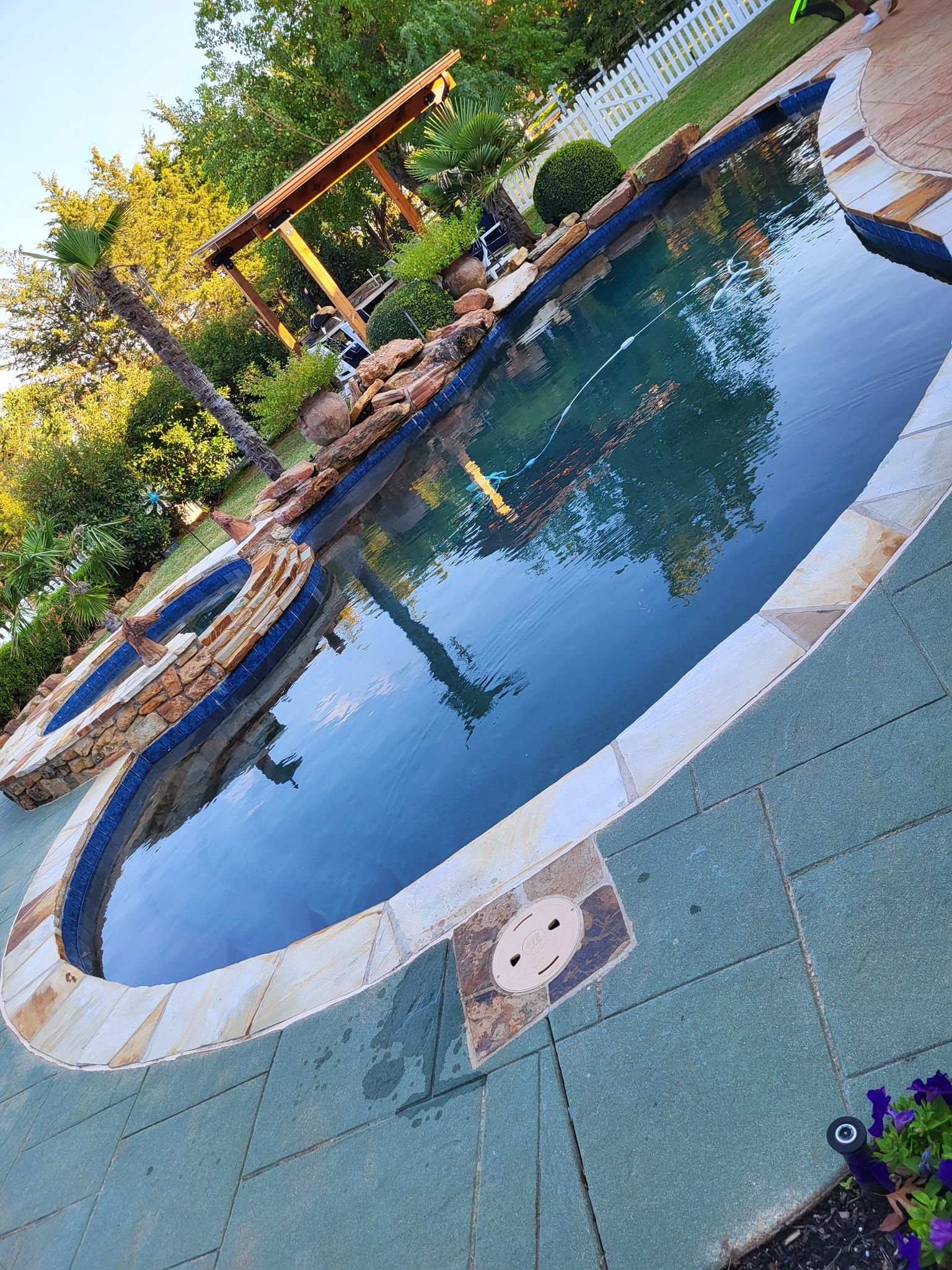 Pool with stone surround and waterfall feature; outdoor setting with greenery.