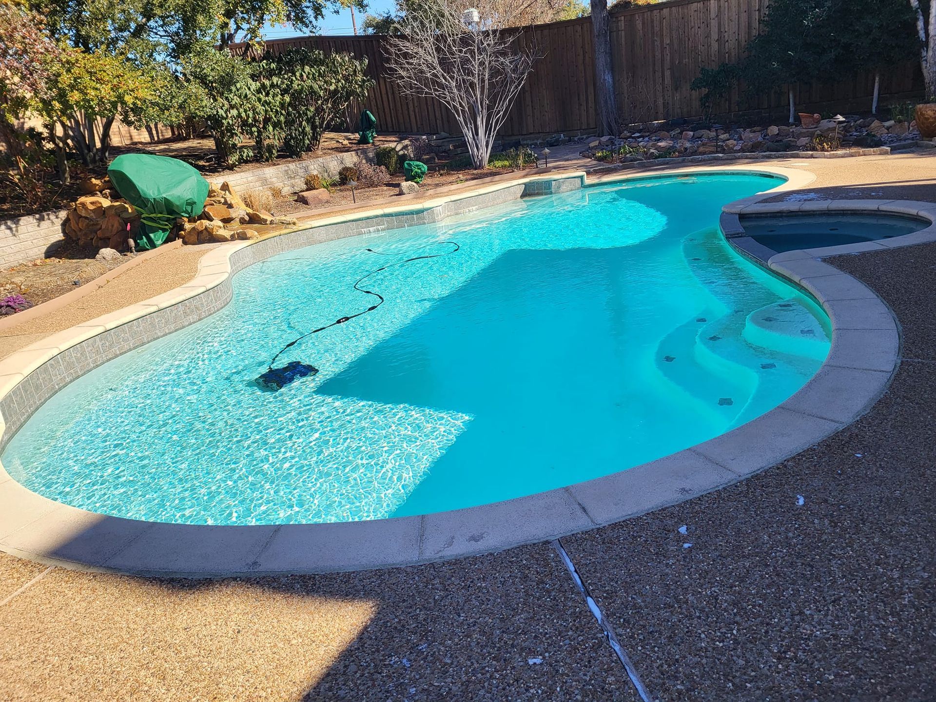 A blue-tiled swimming pool and spa surrounded by stone, with landscaping in the background.