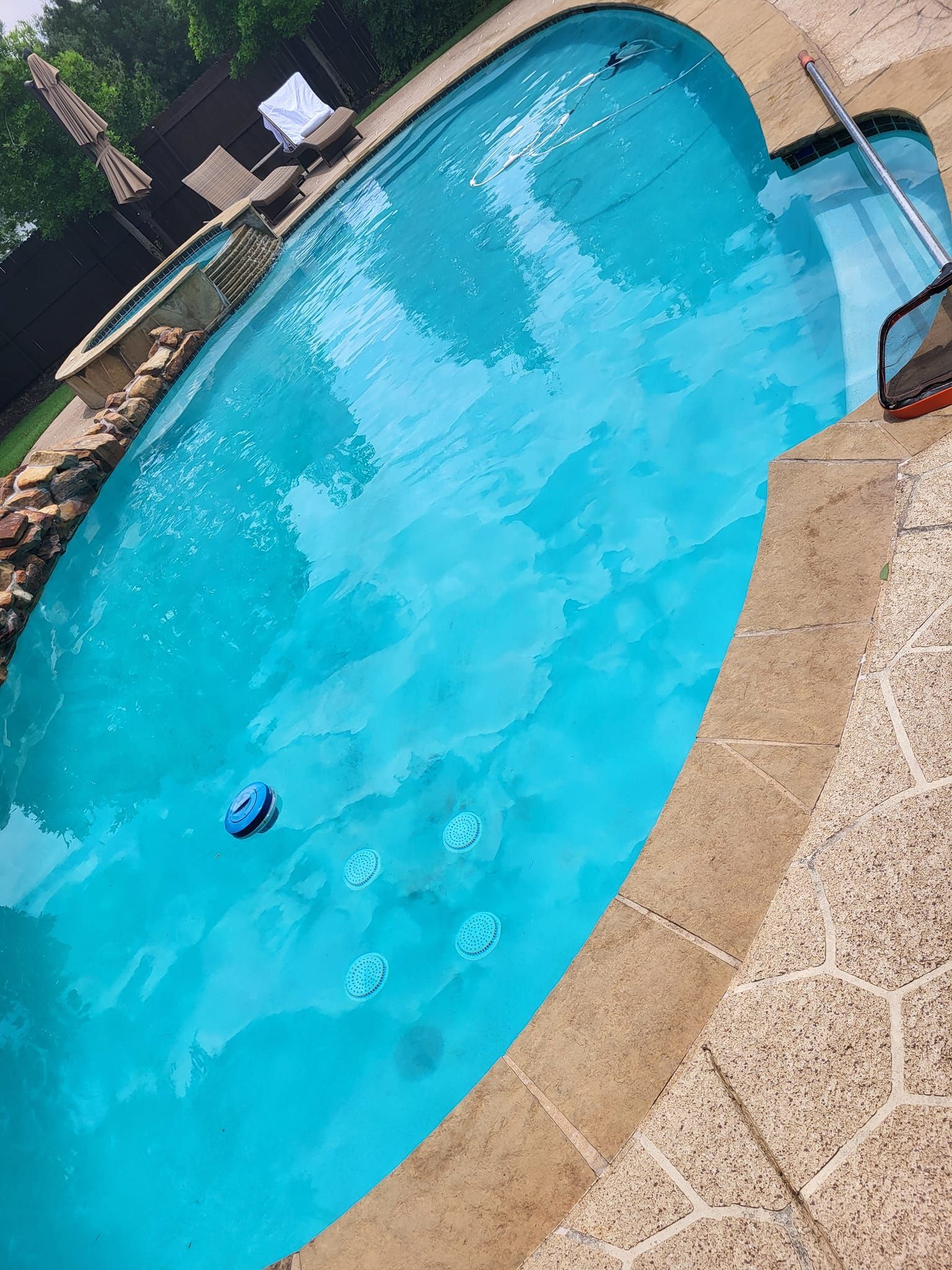 Blue swimming pool with stone coping and a robotic cleaner.