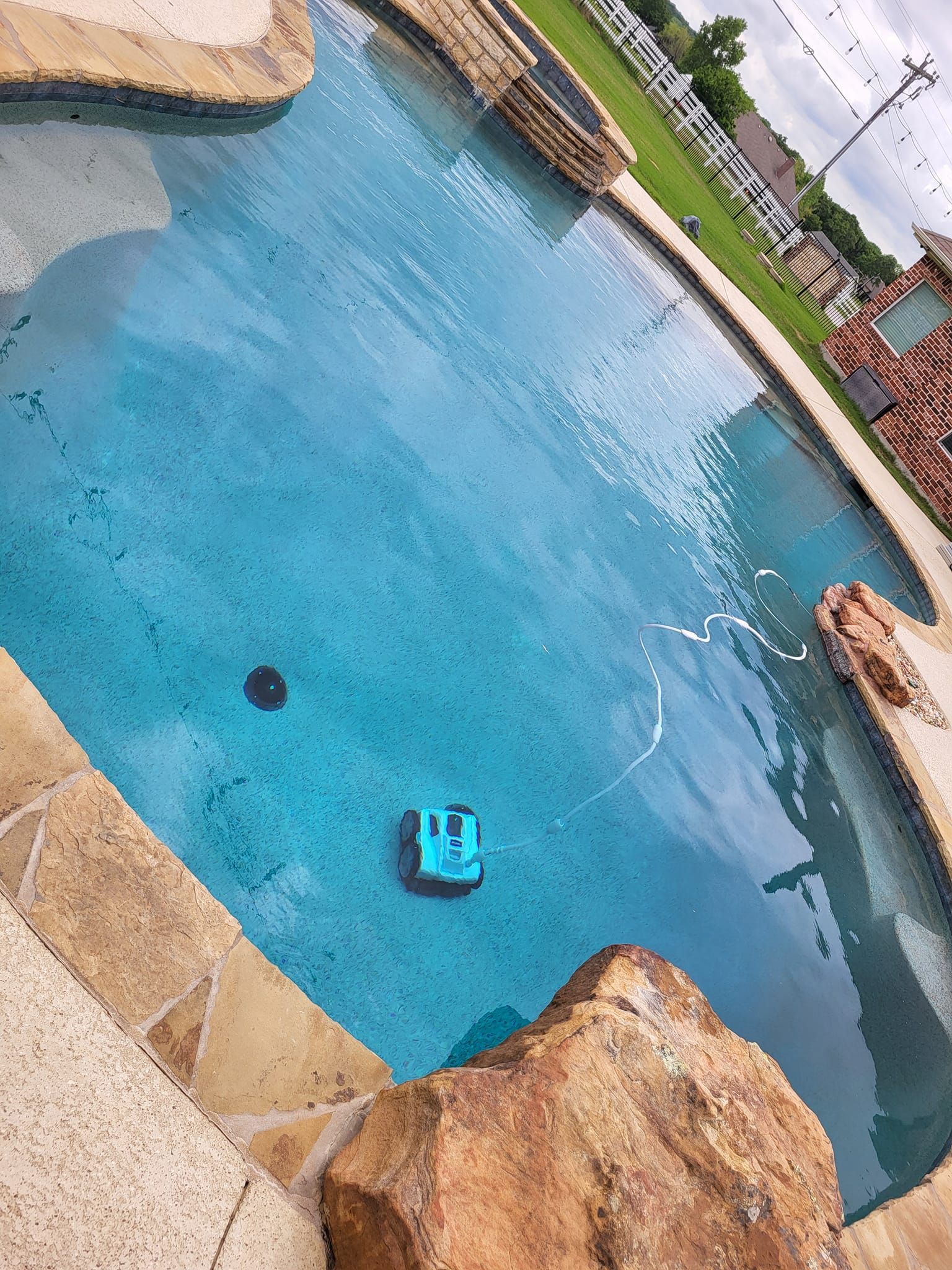 A swimming pool with blue water. A blue robot cleaner is in the pool. Stone border.