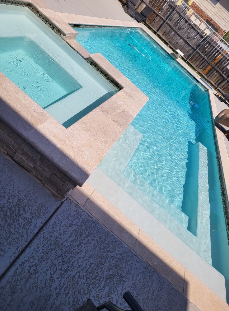 Swimming pool and spa with light blue water and stone borders, outdoors.