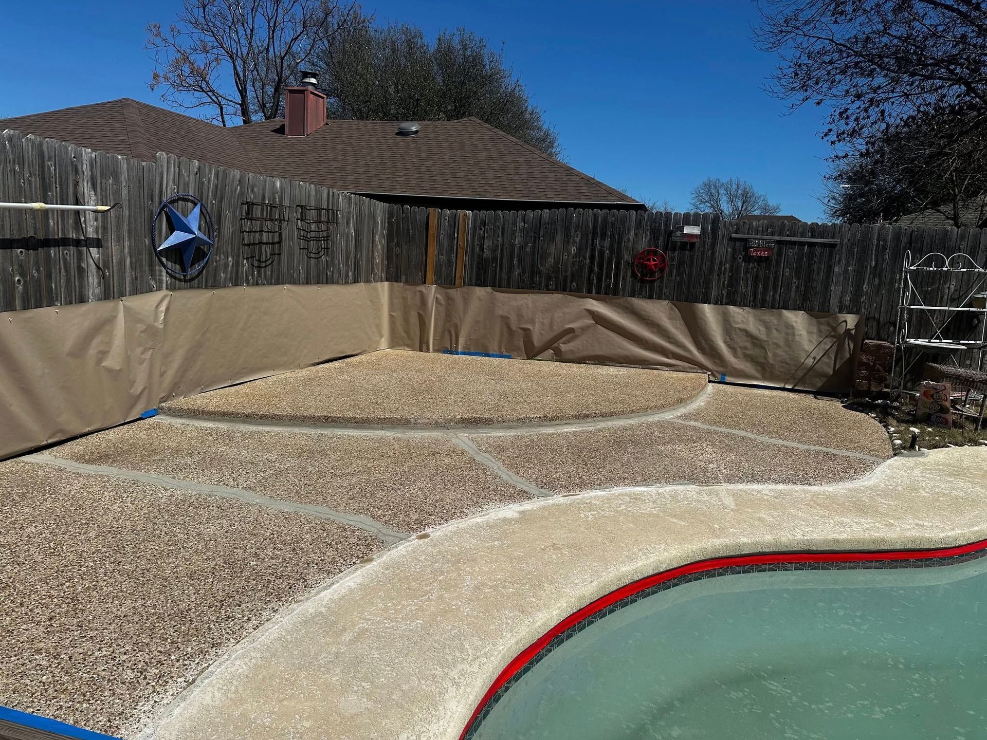 A gravel patio area surrounding a swimming pool with a wooden fence in the background.