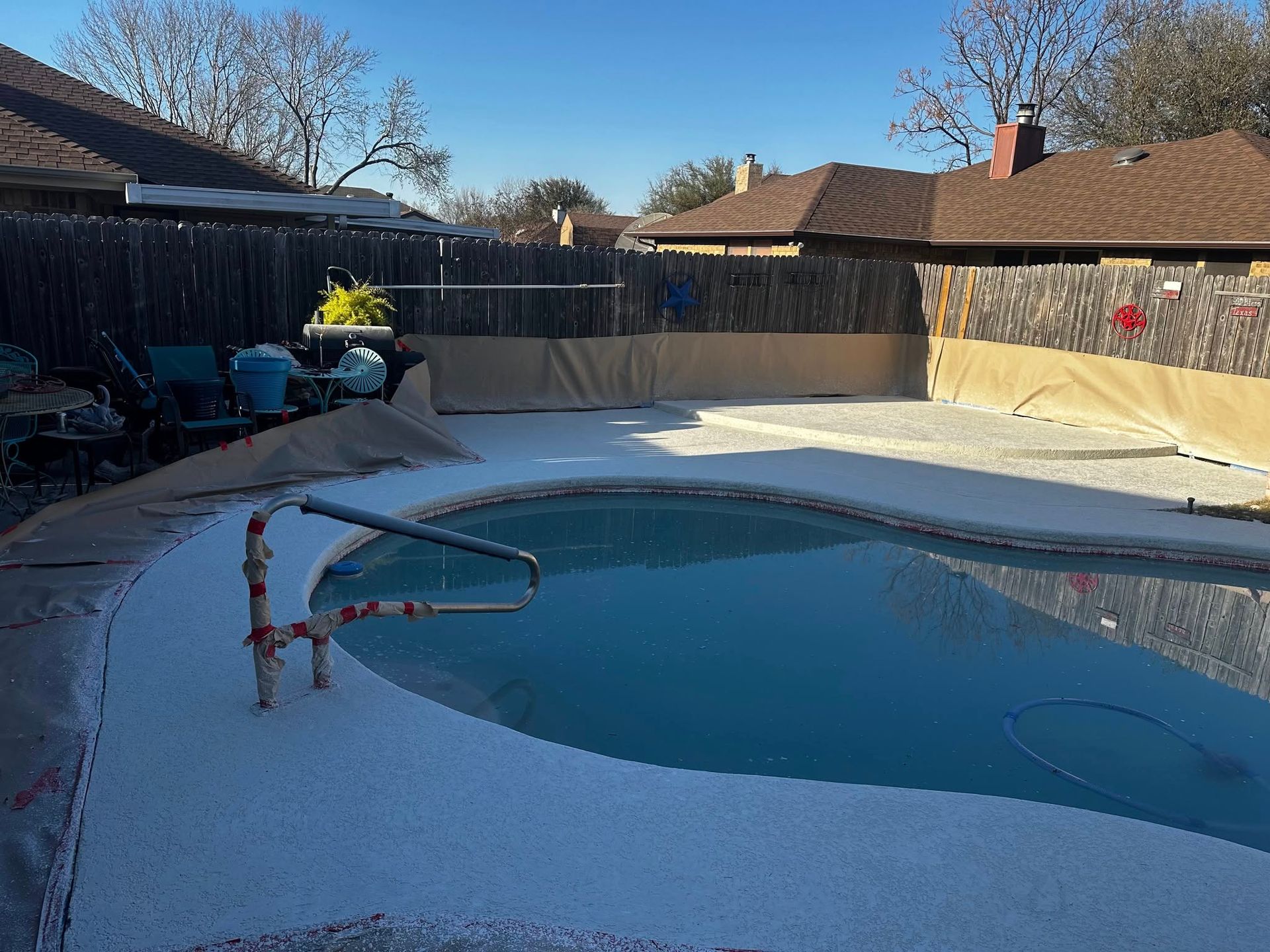Pool with white deck in backyard; brown fence, sunny day.