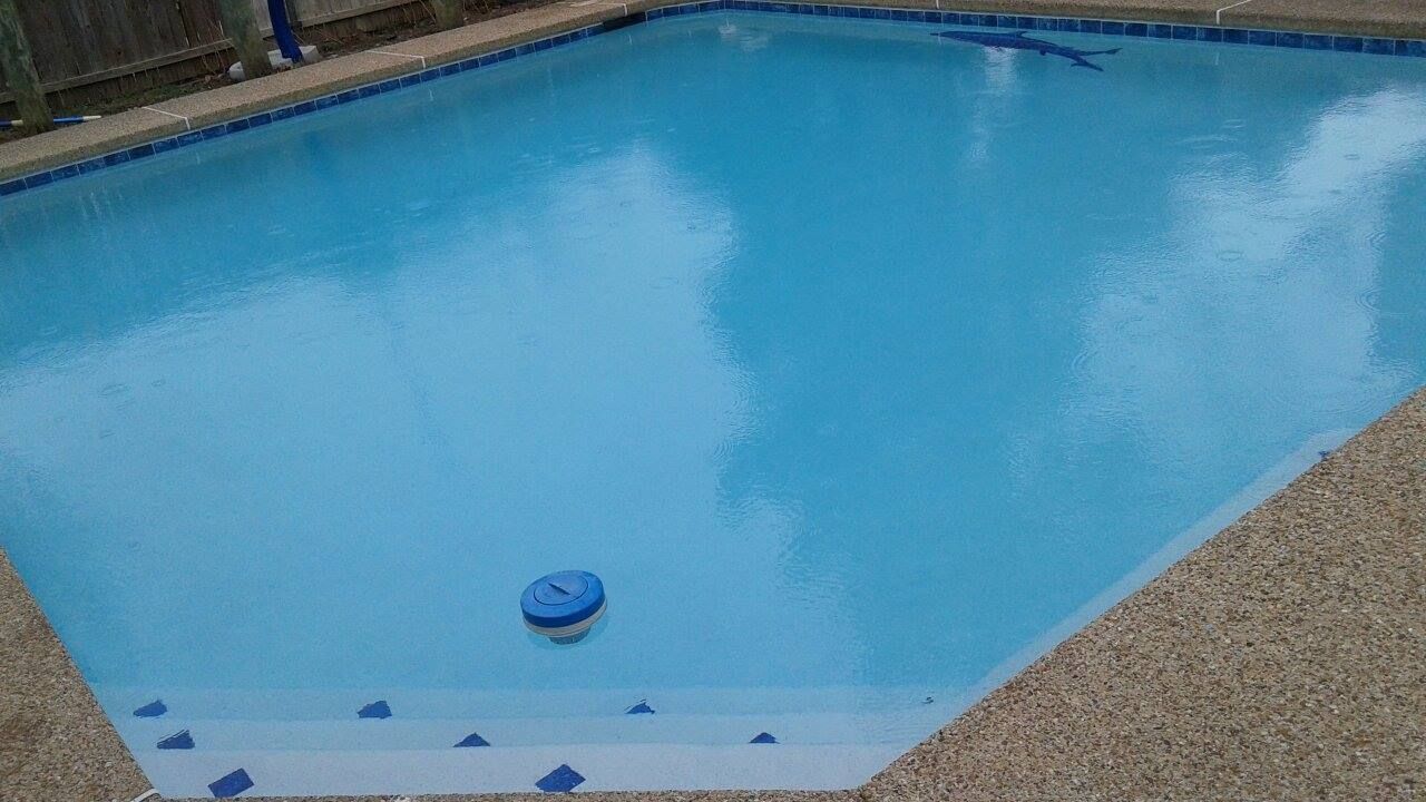 Blue pool with steps, a floating cleaning device, and speckled concrete surround.
