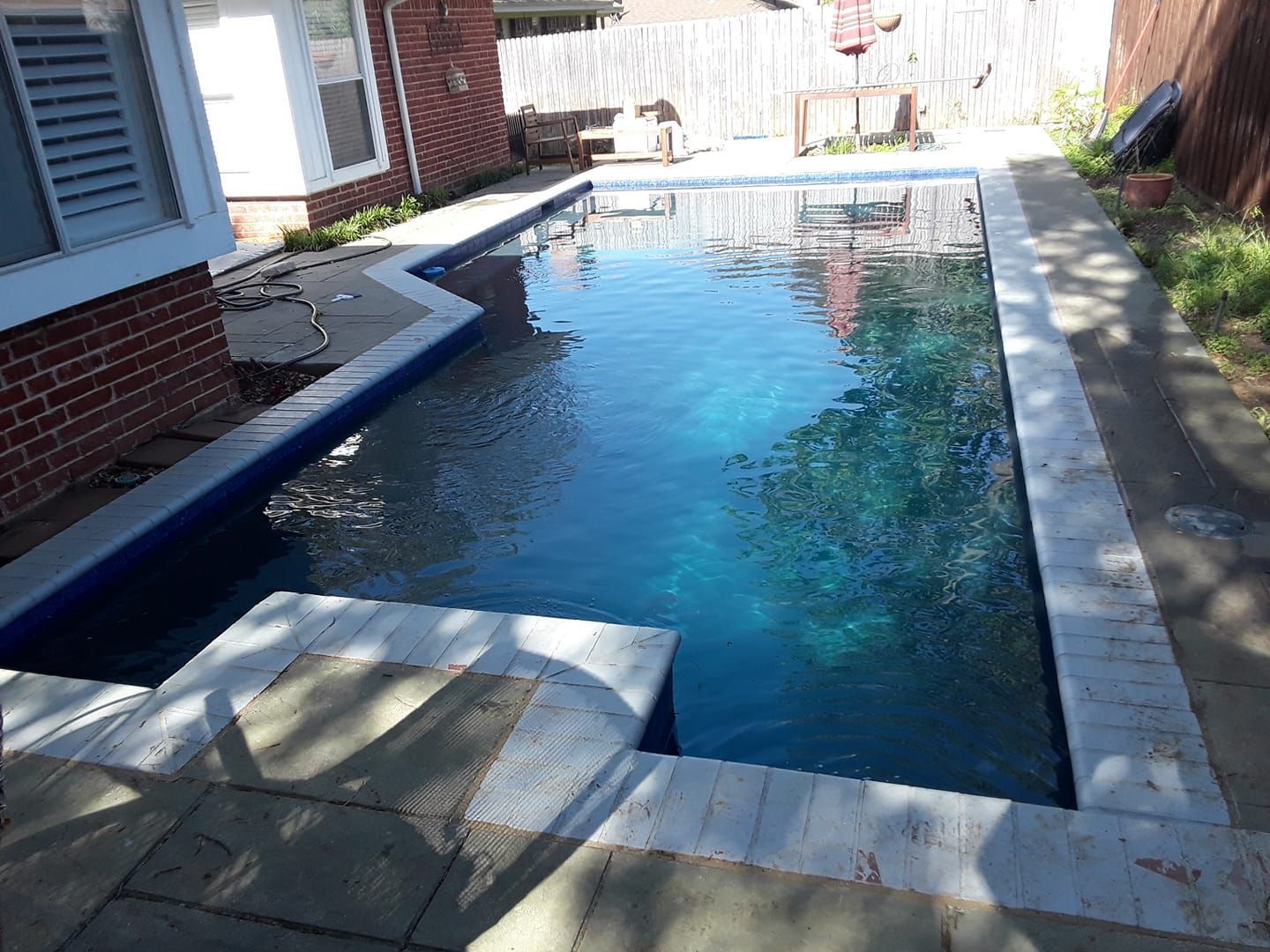 Rectangular backyard swimming pool with blue water, surrounded by concrete and brick walls.