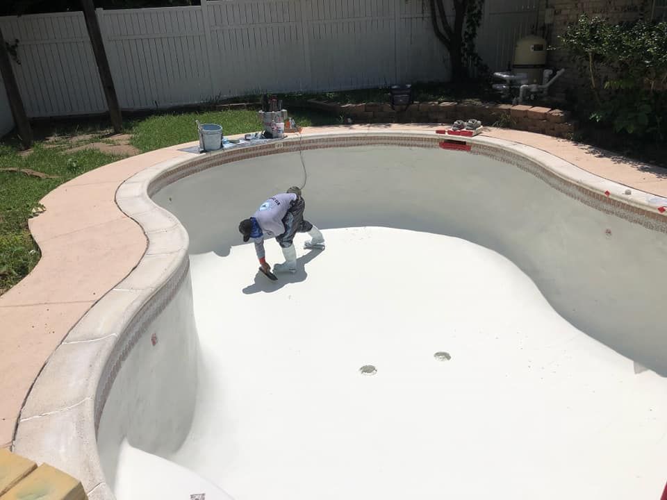 Person painting the interior of an empty, white swimming pool in a backyard.