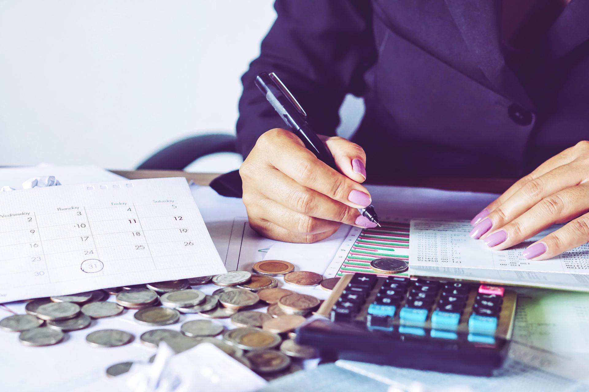 A woman is sitting at a table using a calculator and writing on a piece of paper.