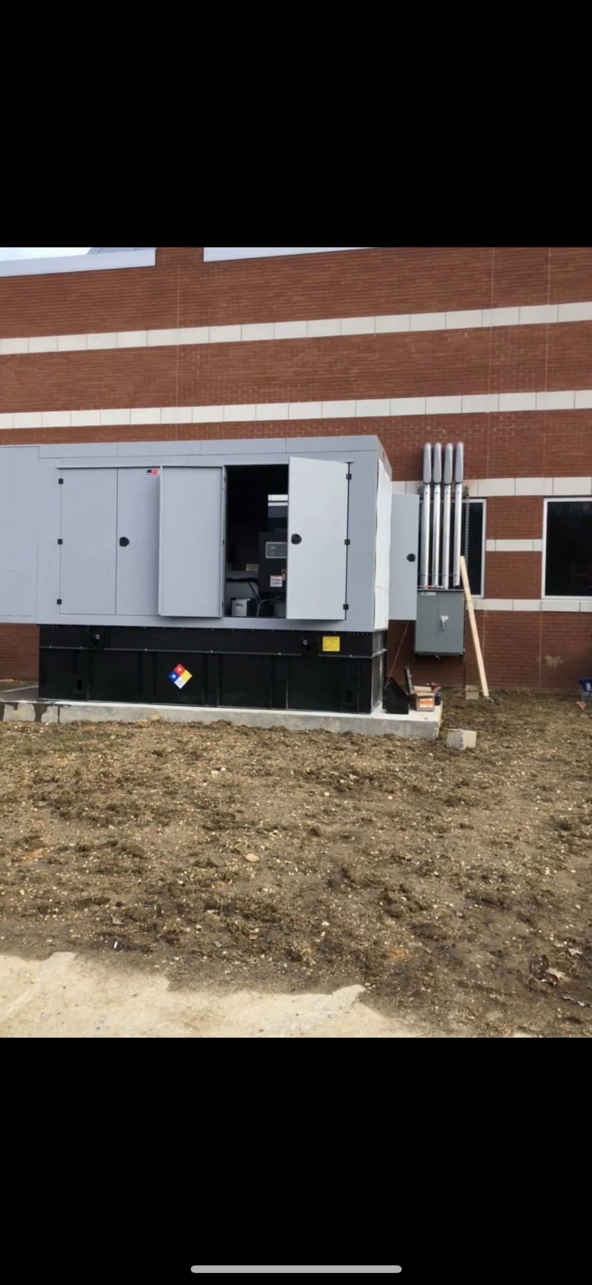 A large generator is sitting outside of a brick building.